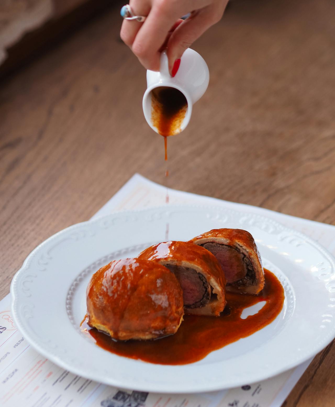 A woman pouring sauce on a plate of meat dish | Source: Pexels