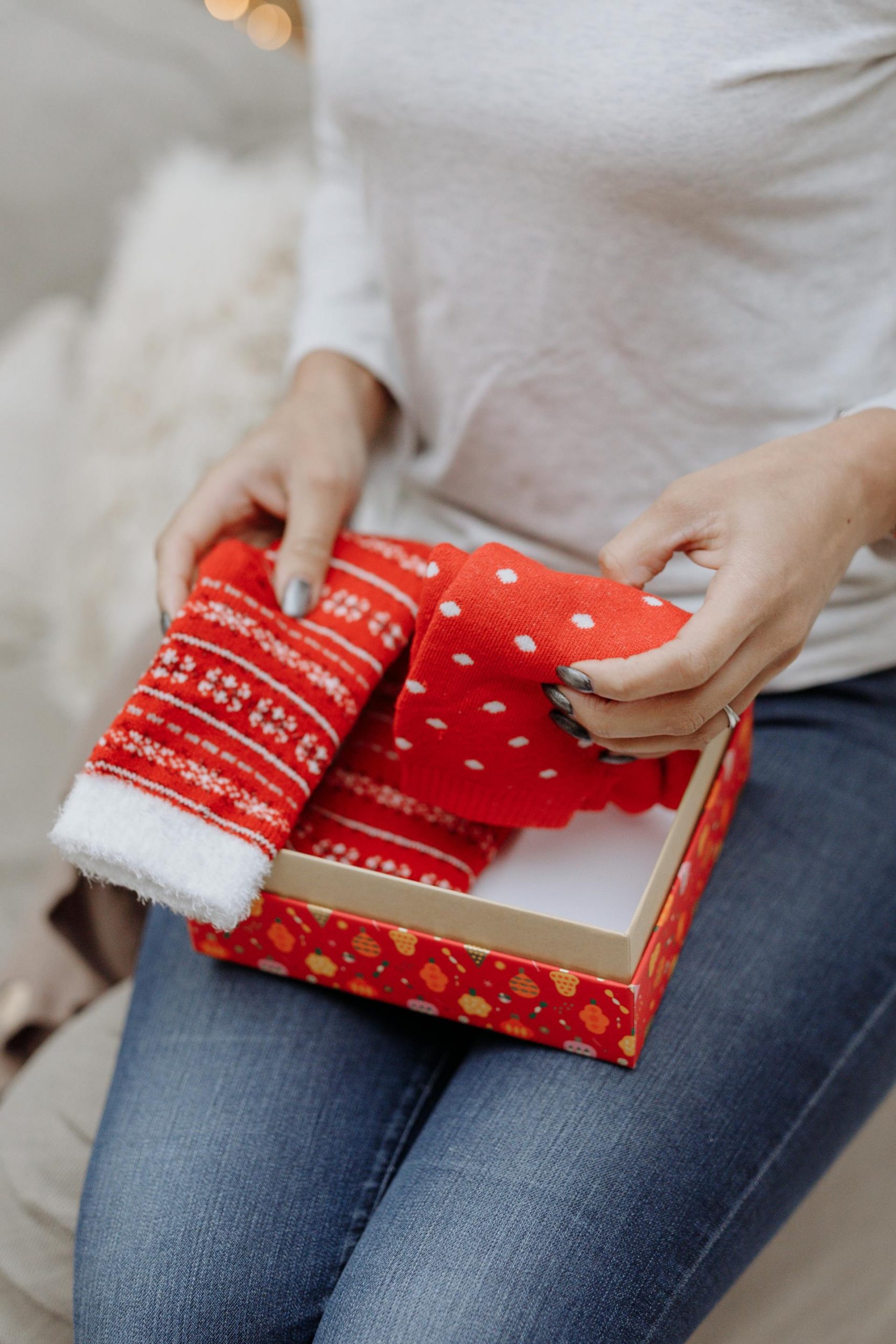 A closeup shot of a woman holding Christmas socks lying a red gift box | Source: Pexels
