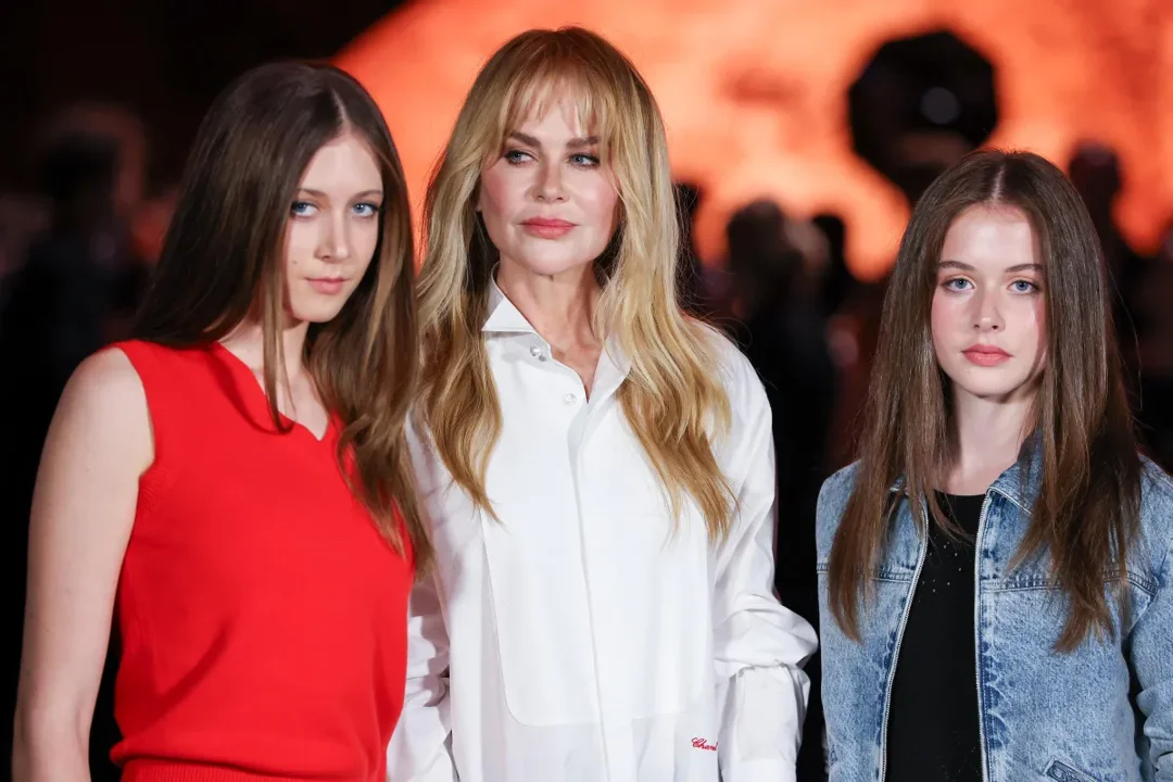 Nicole Kidman appears poised alongside her teenage daughters at the Chanel Womenswear Spring/Summer 2026 show in Paris. The trio faces cameras under the event's warm, glowing light.