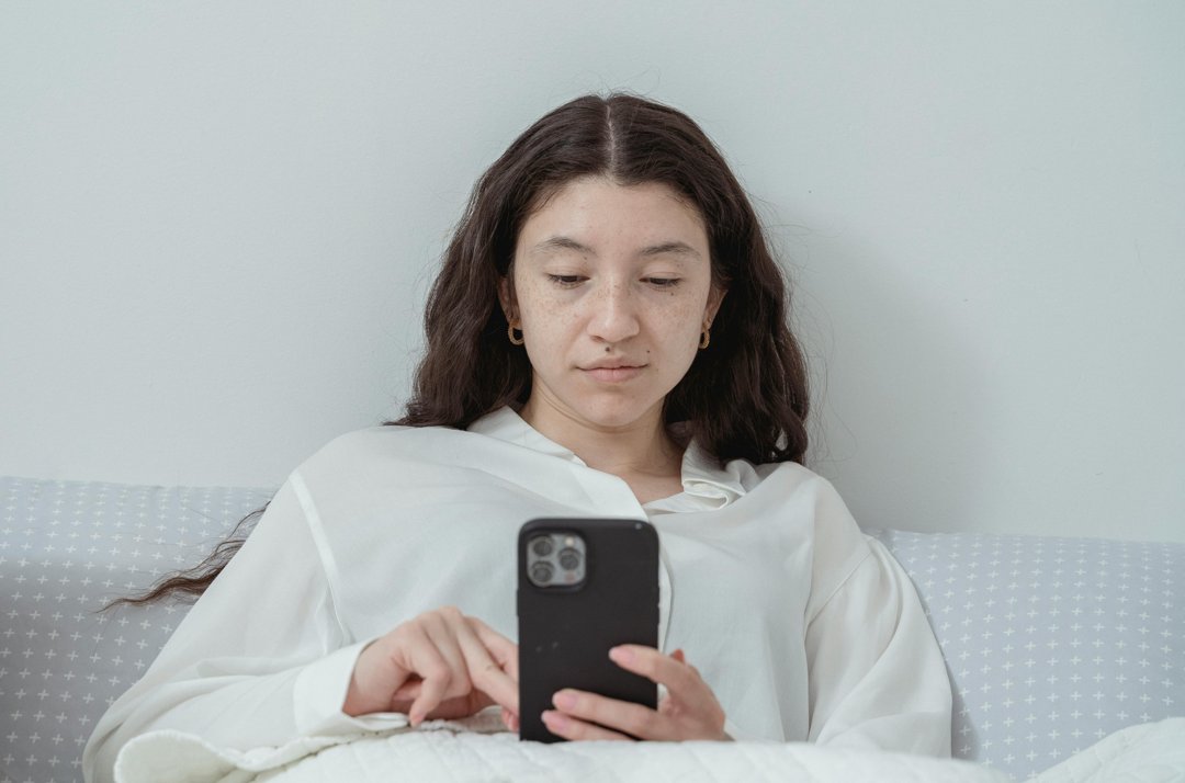 A serious woman using her phone while lying in bed | Source: Pexels