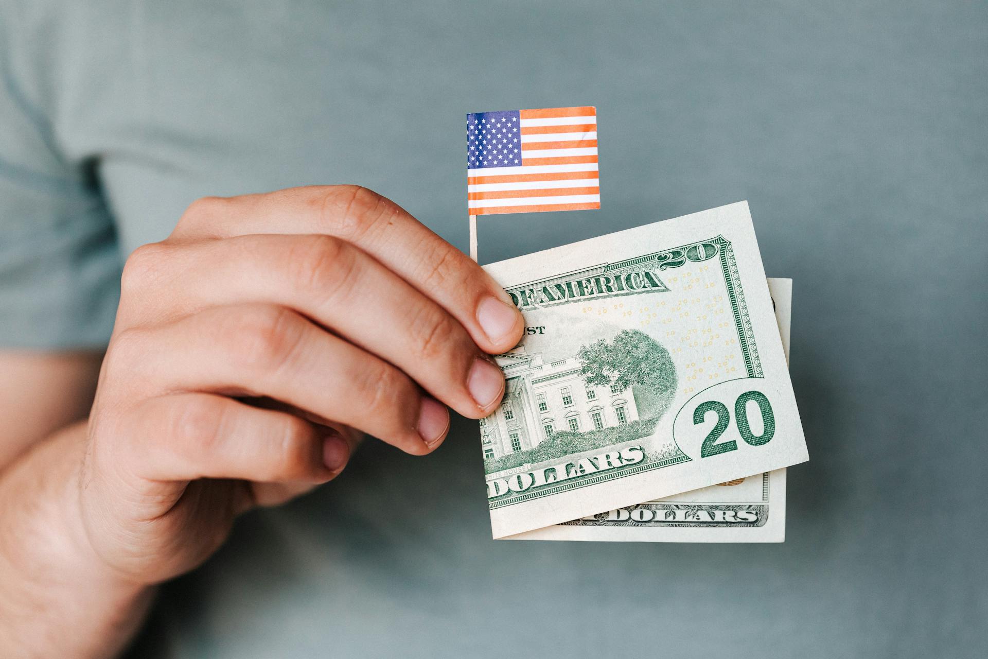 A man holding a $20 bill and a miniature USA flag | Source: Pexels
