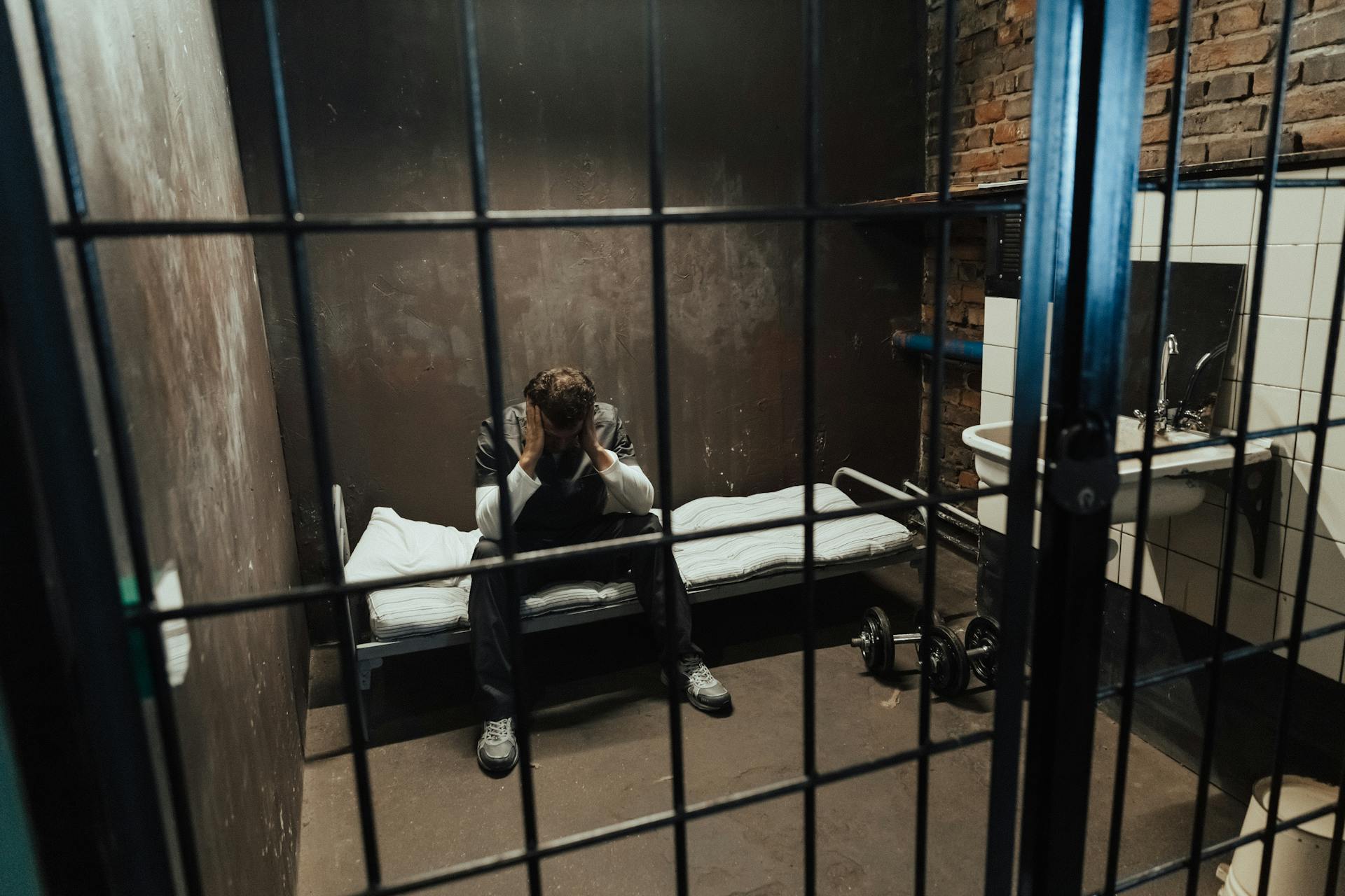 A man sitting on a bed behind bars | Source: Pexels