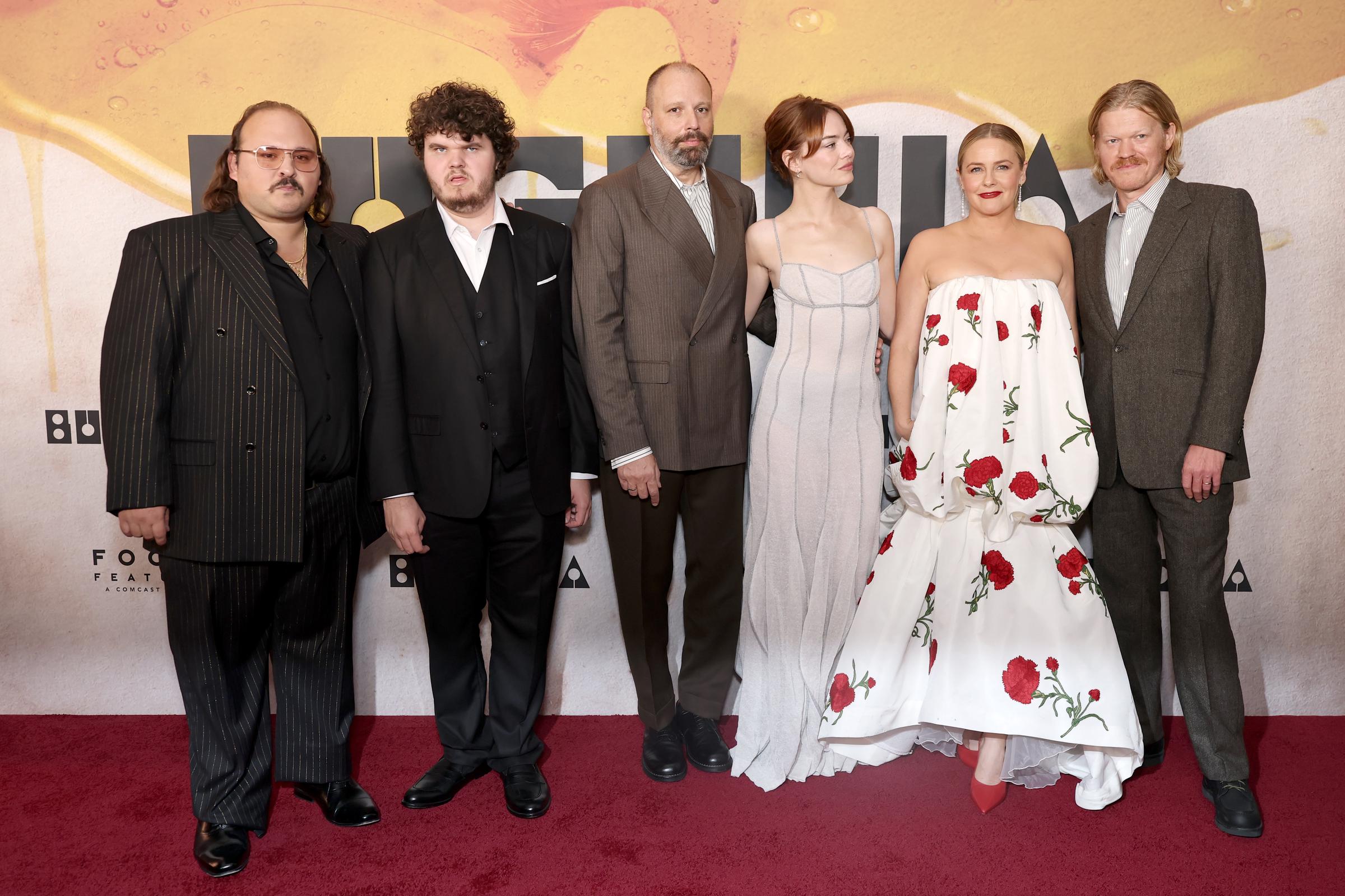 With her gaze turned slightly away from the camera, Emma Stone stands alongside her “Bugonia” co-stars Stavros Halkias, Aidan Delbis, Alicia Silverstone, Jesse Plemons, and director Yorgos Lanthimos, her gown standing out amid the group's tailored looks.