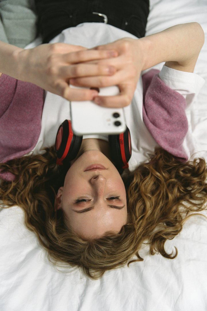 A woman using her phone while lying on a bed | Source: Pexels
