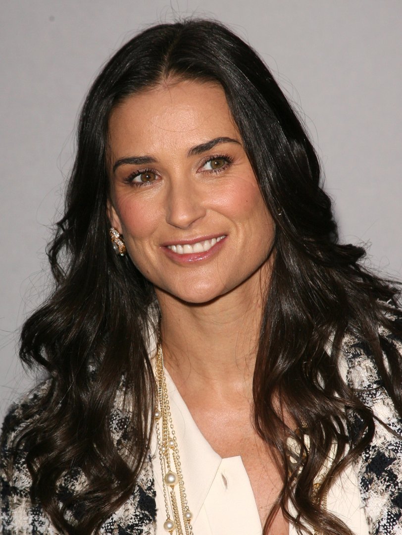 Radiating timeless grace, she smiles with quiet confidence, her cascading dark hair framing a face that glows with poise. Draped in pearls and textured elegance, she embodies sophistication. Demi Moore stands as a portrait of enduring beauty—refined, natural, and effortlessly captivating.