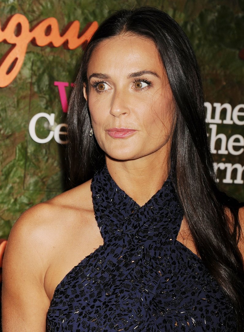 Bathed in warm light, Demi Moore exudes quiet strength and refined allure, her gaze both poised and enigmatic. The intricate navy gown shimmers subtly, mirroring her understated elegance. She stands as a vision of timeless beauty