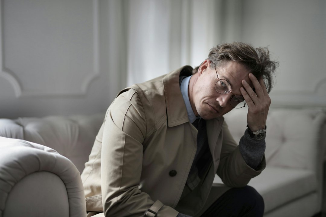 A man sitting on a couch and holding his head | Source: Pexels