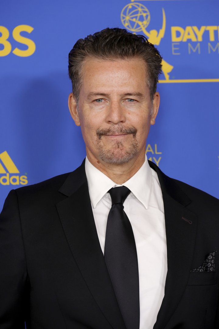 Ted King appears at the Daytime Emmy Awards in 2022, dressed in a classic black suit and tie with a white shirt. His neatly styled hair and trimmed goatee complement the formal setting, while the Emmy backdrop reinforces the celebratory nature of the occasion.