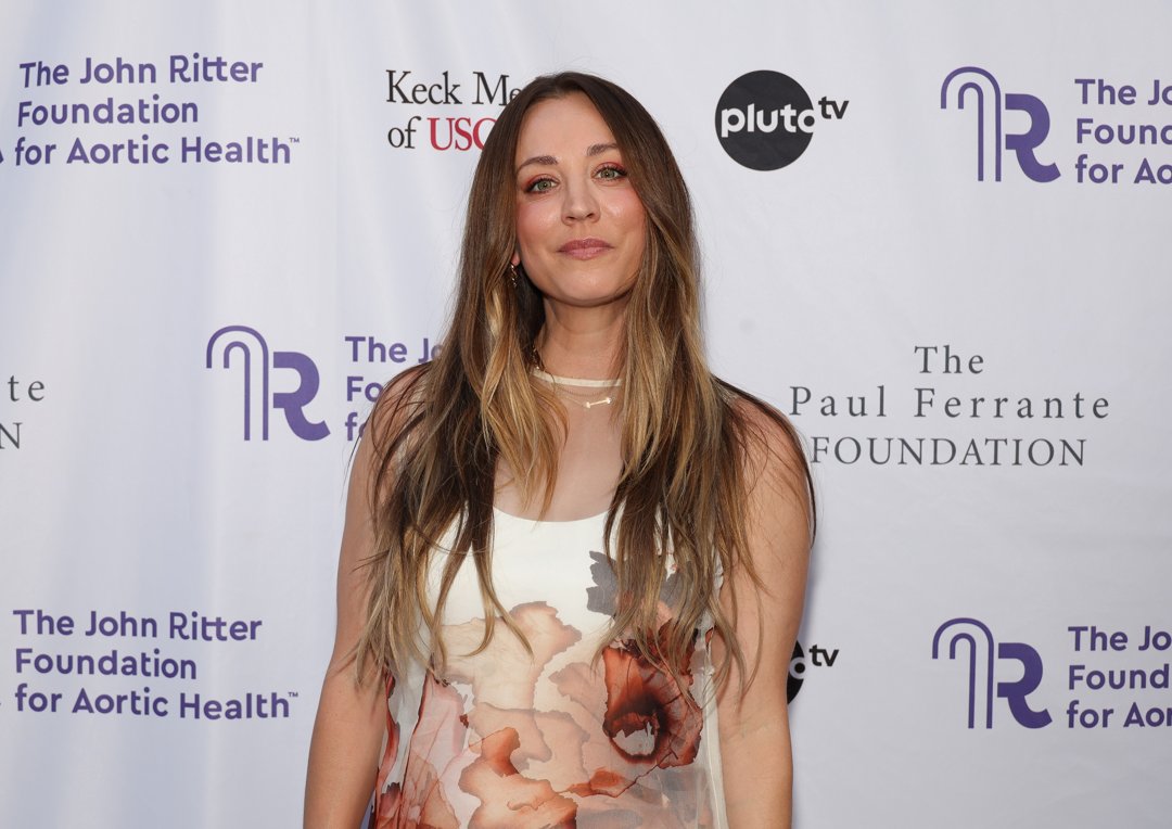 Kaley Cuoco attends the John Ritter Foundation event in a sheer floral-print dress with soft pink and red tones. Her long, wavy hair and minimal jewelry give the look a relaxed, elegant vibe.