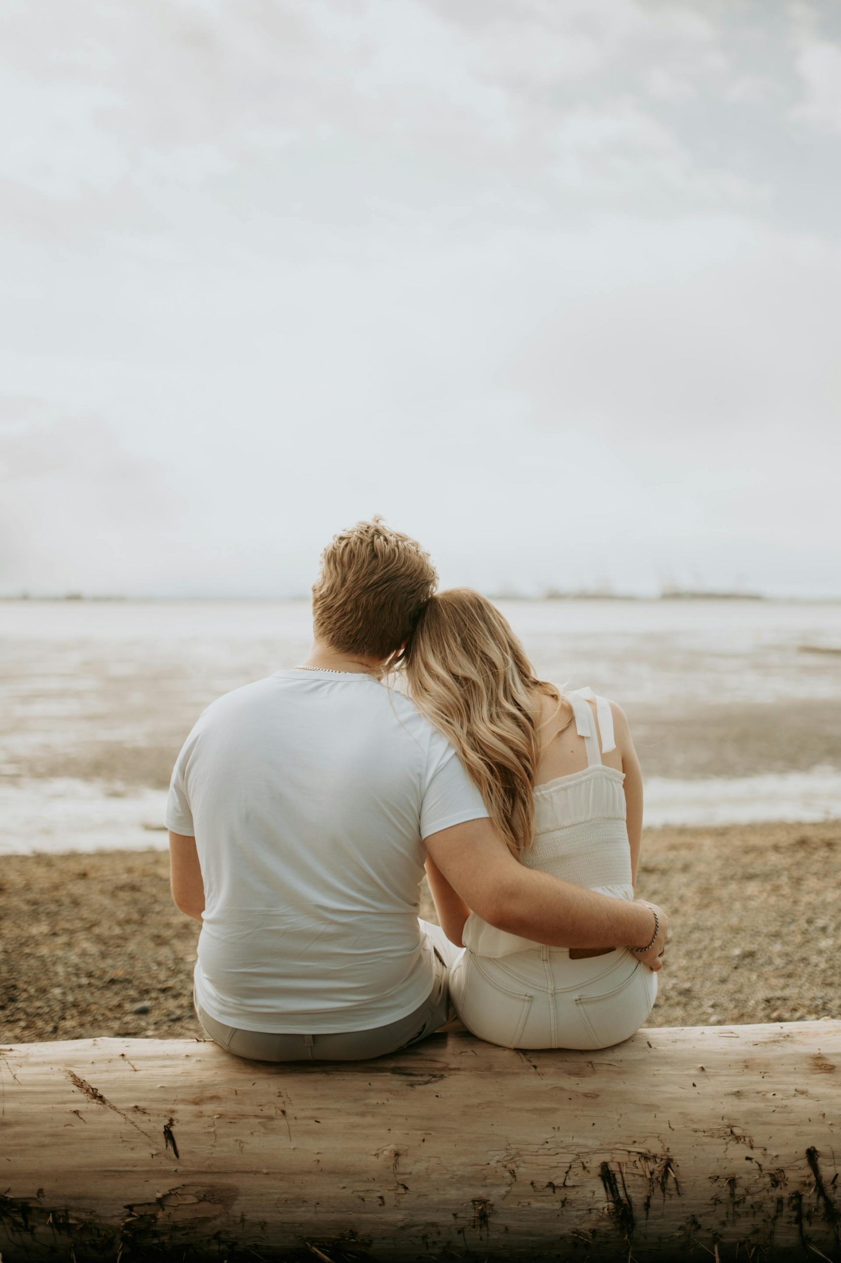 Back view of a couple sharing a hug while sitting on a beach | Source: Pexels
