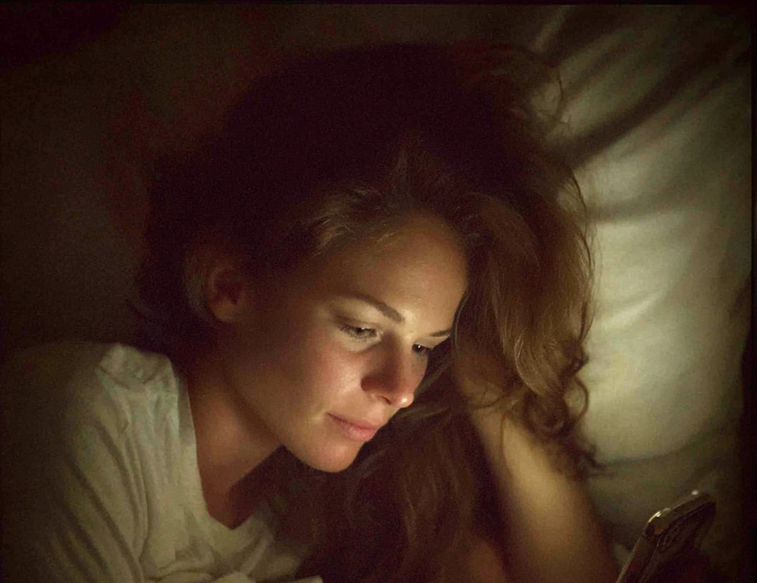 A woman lying in bed and using her phone | Source: Midjourney