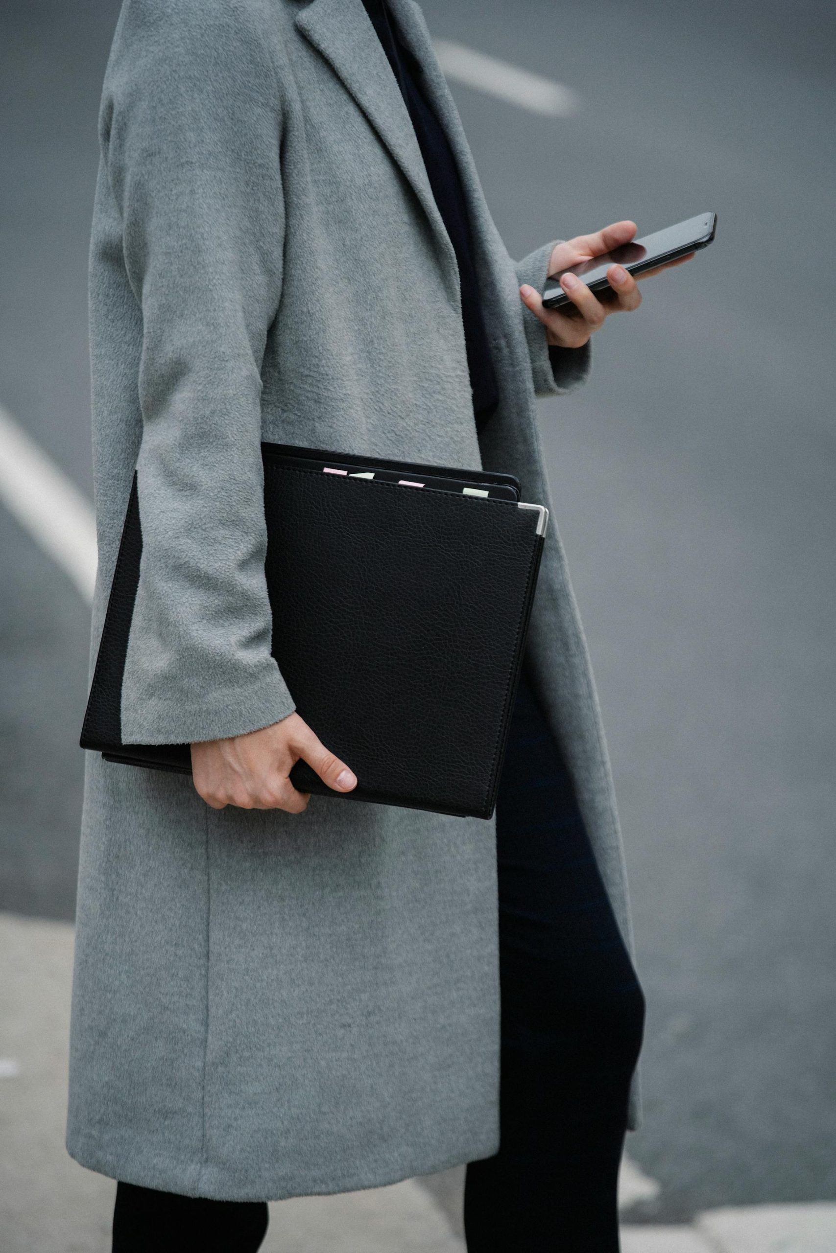 Close-up shot of a woman with a folder and smartphone walking on the road | Source: Pexels
