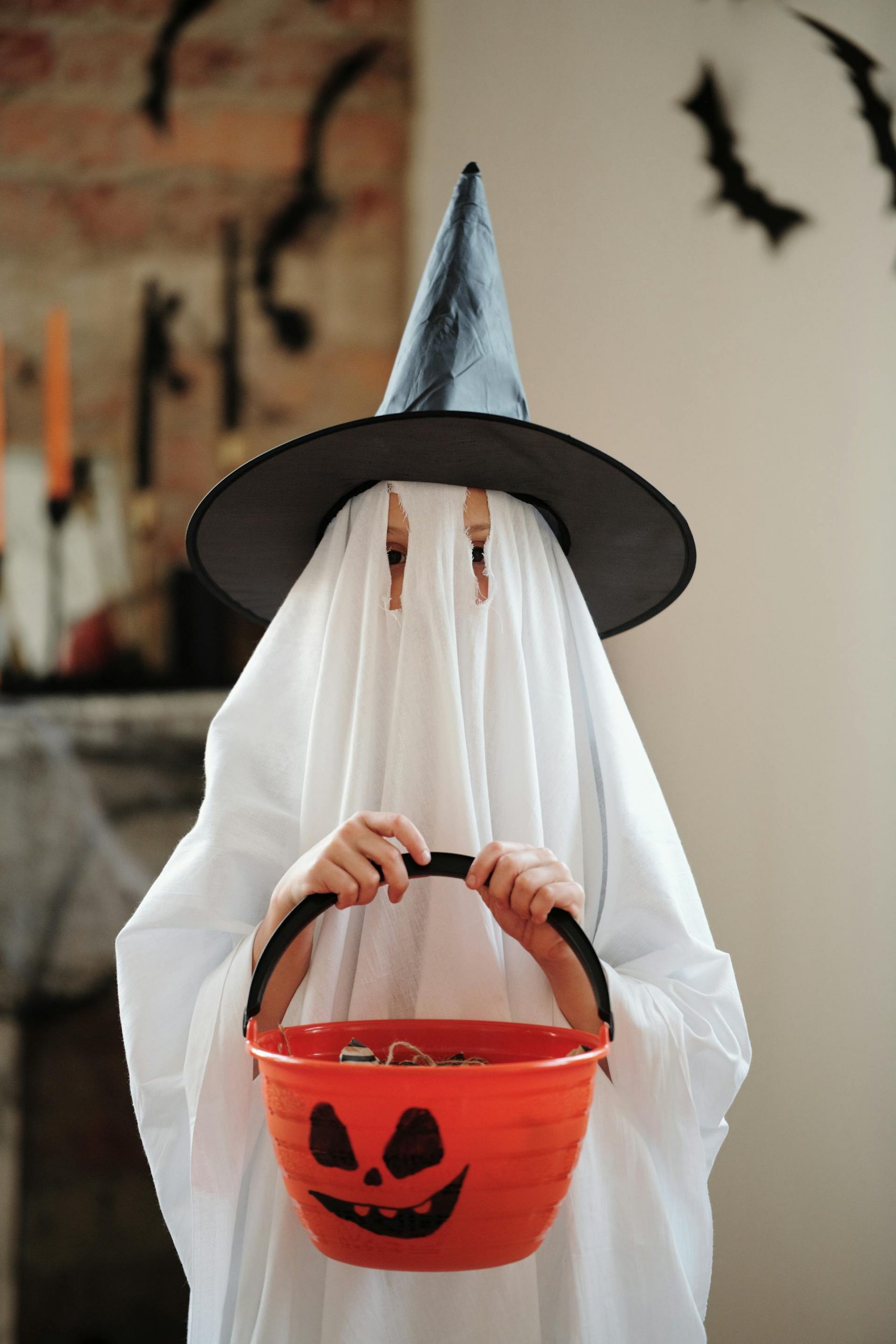 A child in a ghost costume holding a Halloween-themed bucket | Source: Pexels