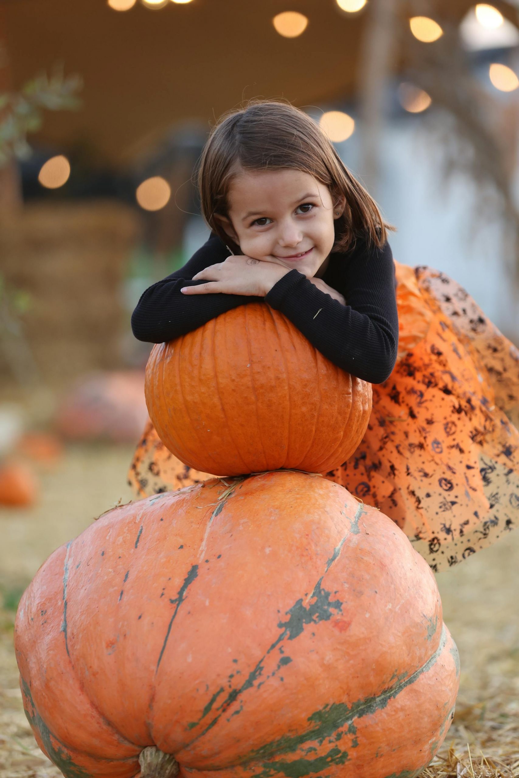 A little girl resting her head on the top of a stack of pumpkins | Source: Pexels