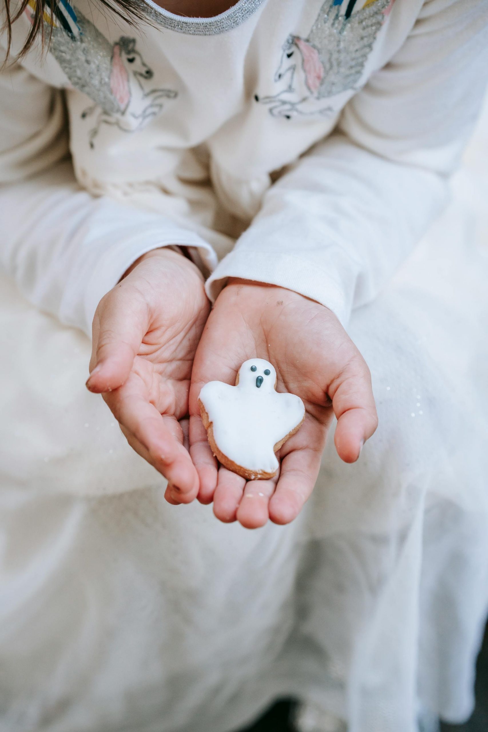 A little girl holding a ghost cookie in her hands | Source: Pexels