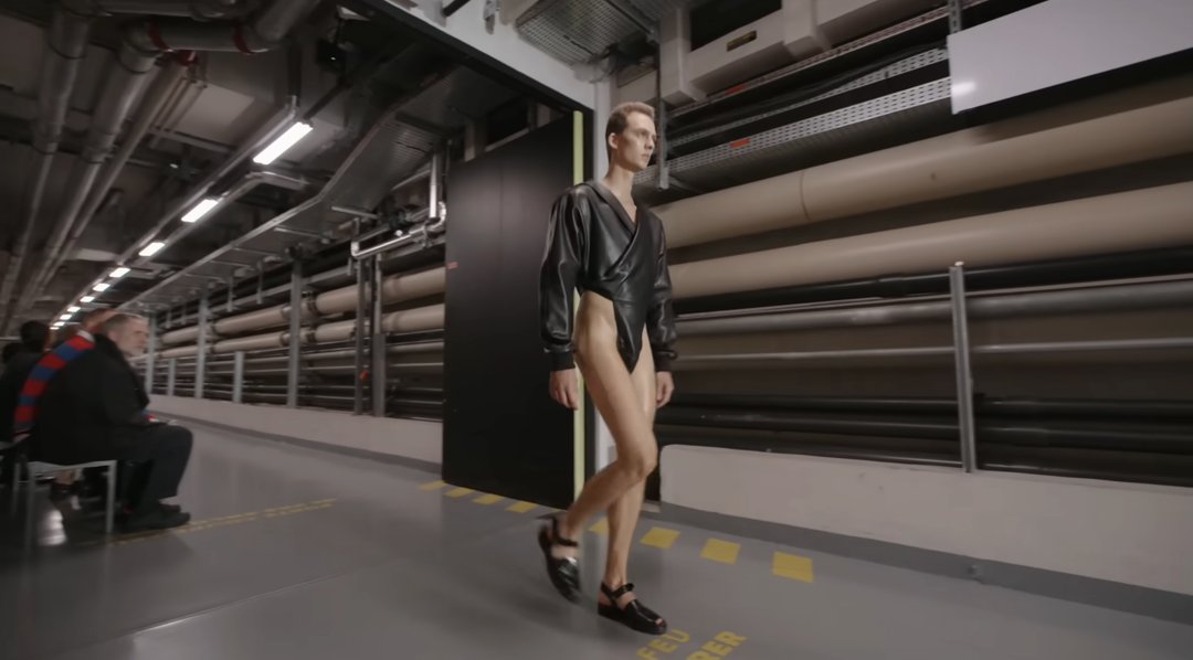 The model rounds the corner, revealing just how high the bodysuit’s cuts go. He pairs the look with black open shoes, adding to the futuristic vibe — a glimpse of what daring fashion might look like in the years ahead. From a post dated October 5, 2025. Source: Youtube/@jeanpaulgaultier