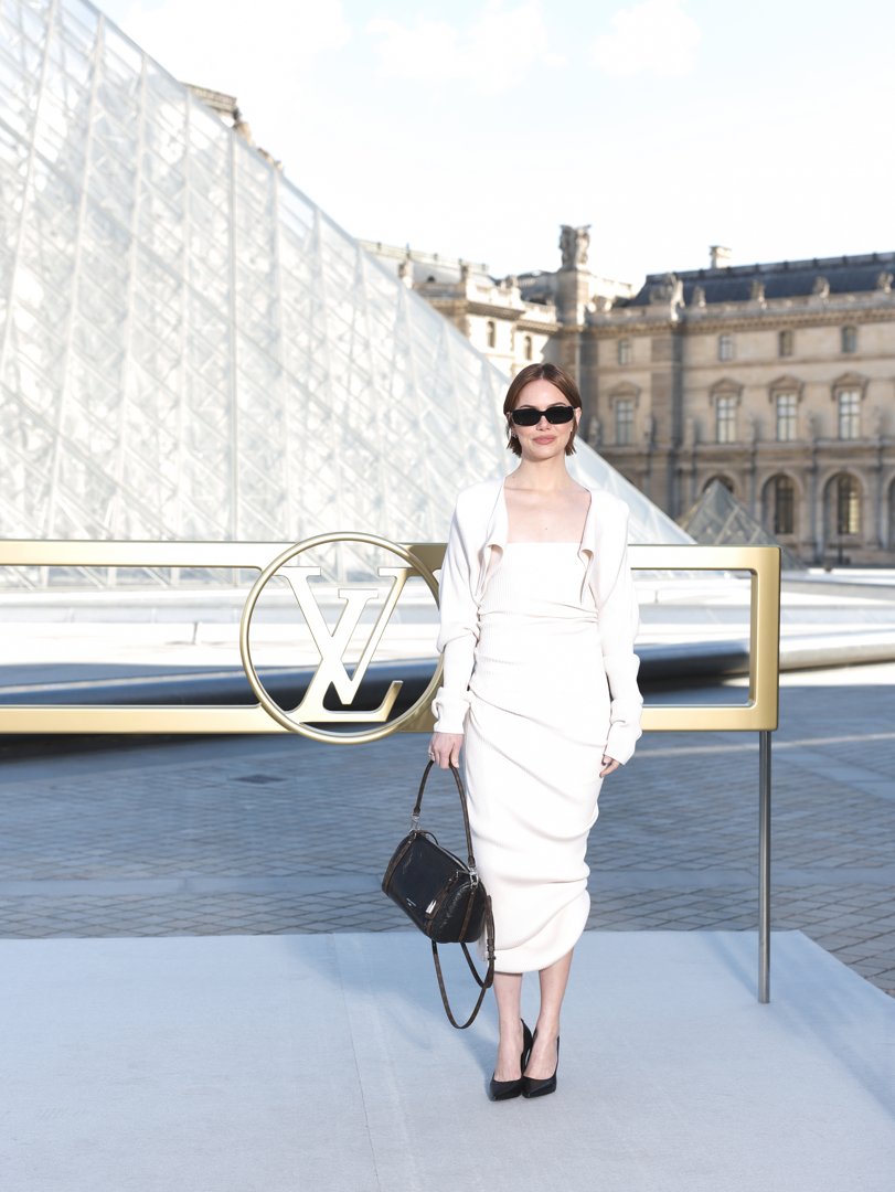 Emma Stone attended the Louis Vuitton Women’s Spring/Summer 2026 show at Paris Fashion Week in France. She wore a creamy white, heavily ribbed midi-length dress that showcased texture and silhouette mastery. It was paired with sharp black accessories to anchor the monochromatic look.