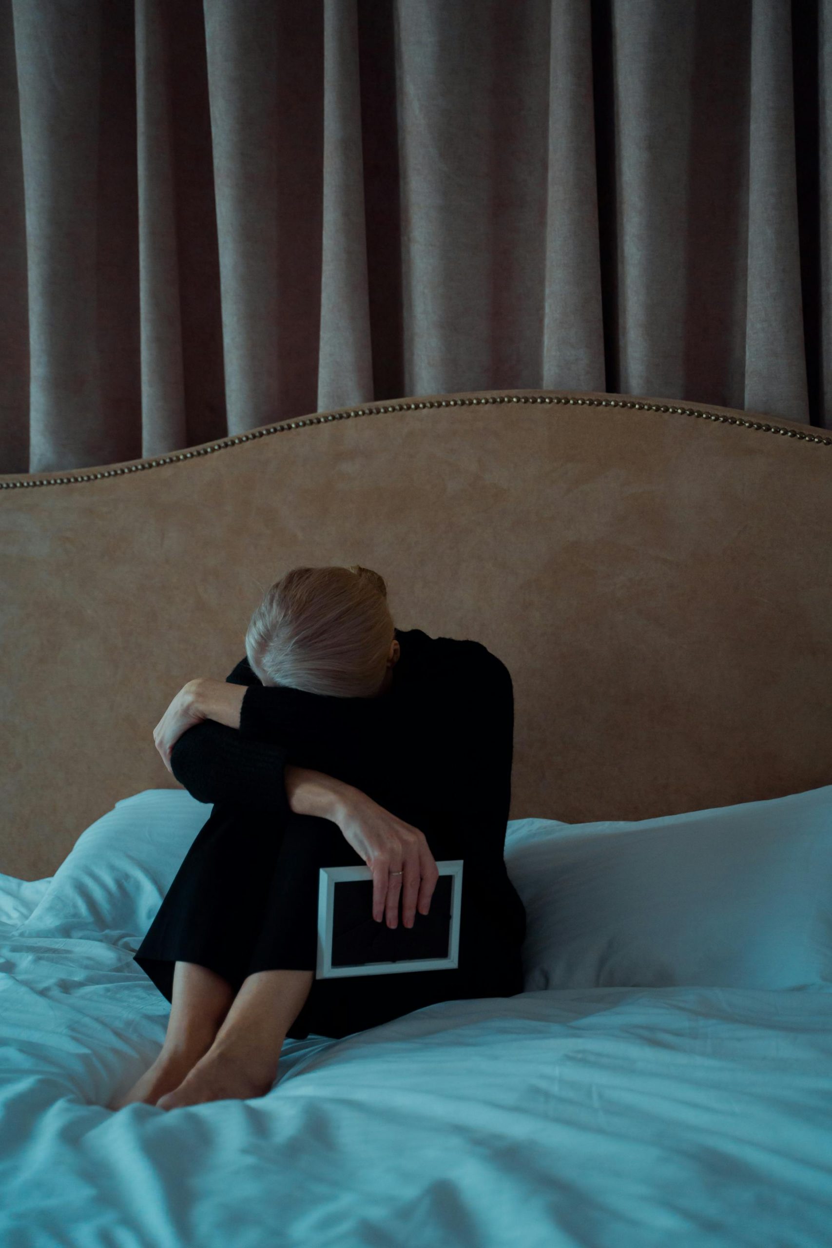 A sad senior woman holding a photo frame while sitting on her bed | Source: Pexels
