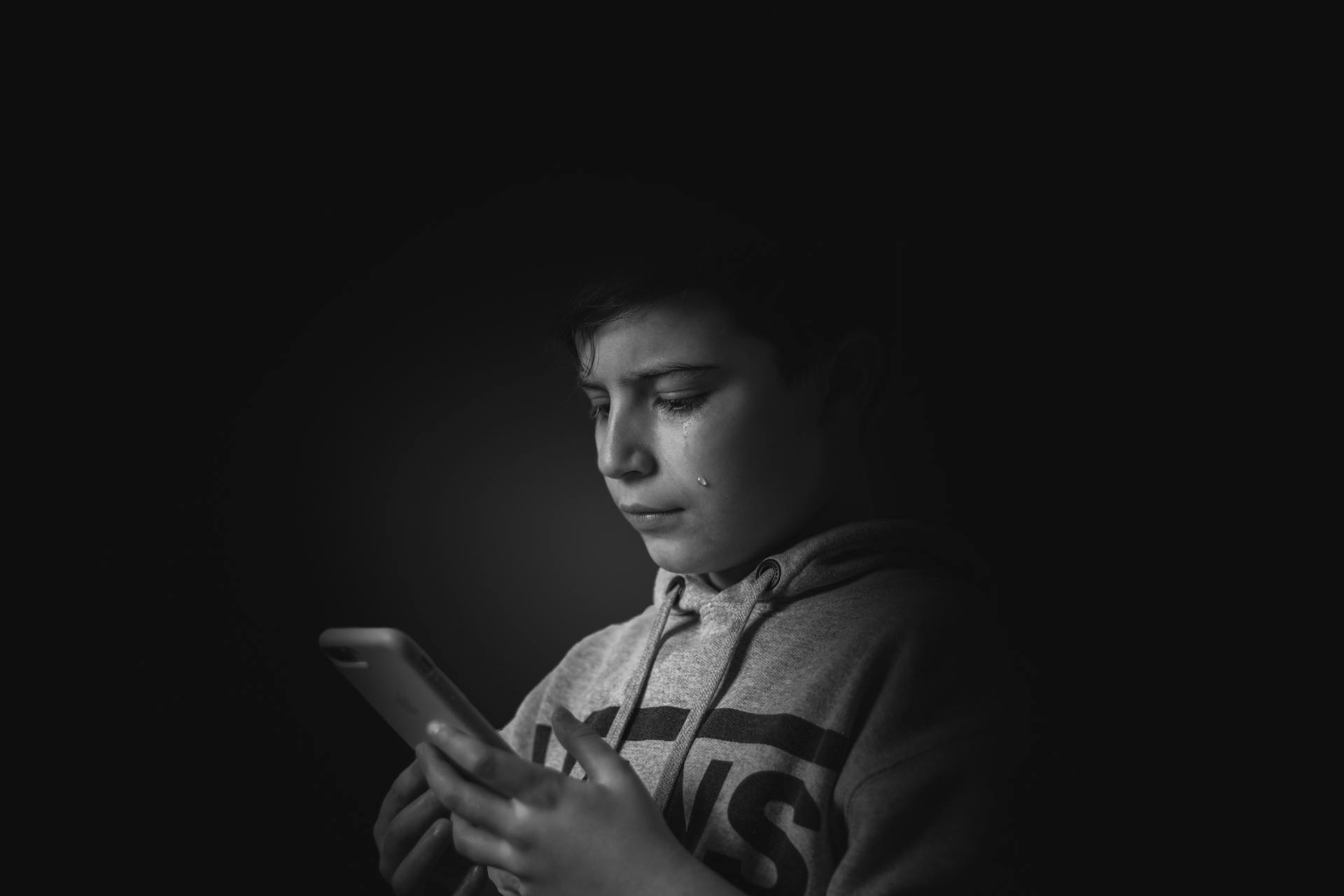 A teary-eyed young boy looking at his phone | Source: Pexels