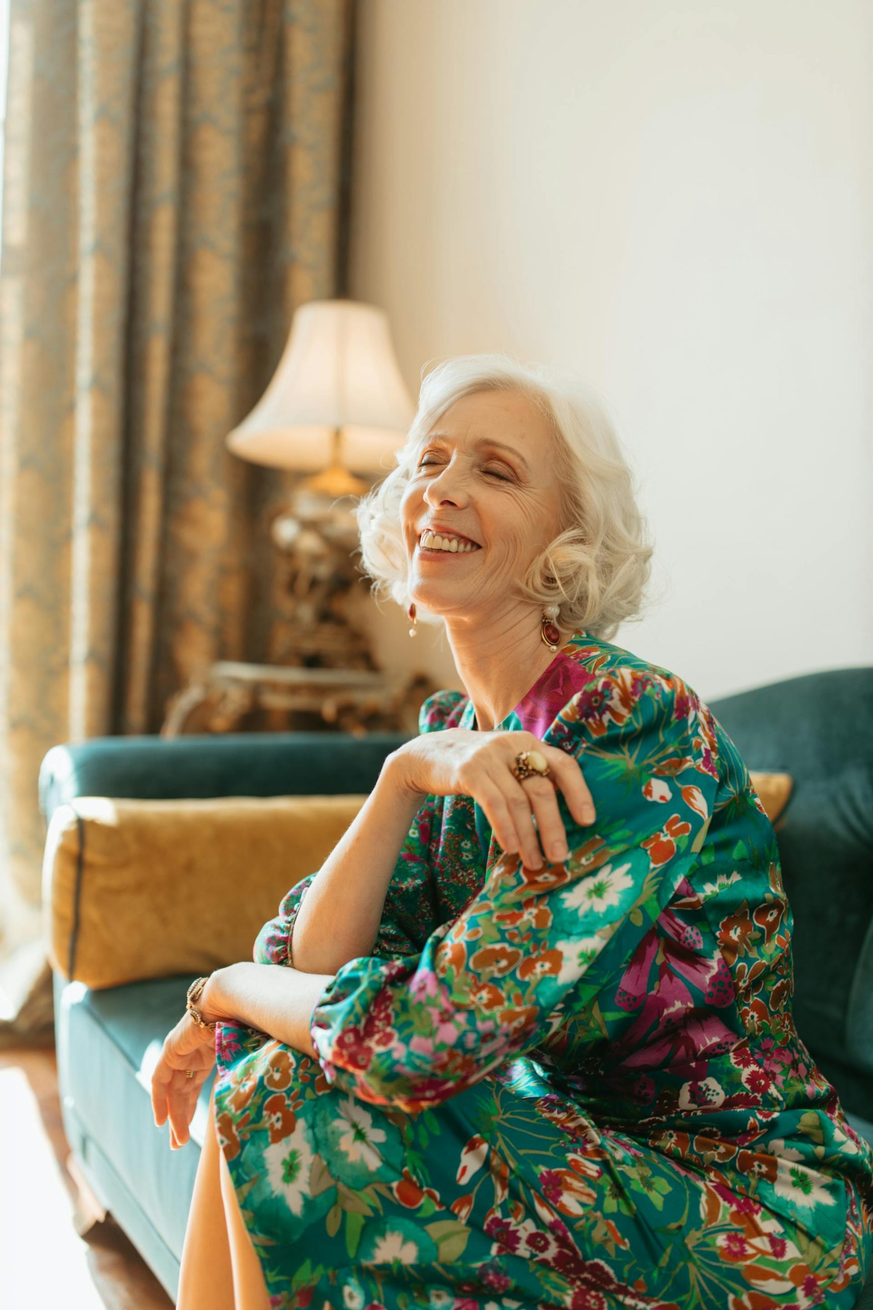 An elderly woman sitting on the couch and laughing | Source: Pexels