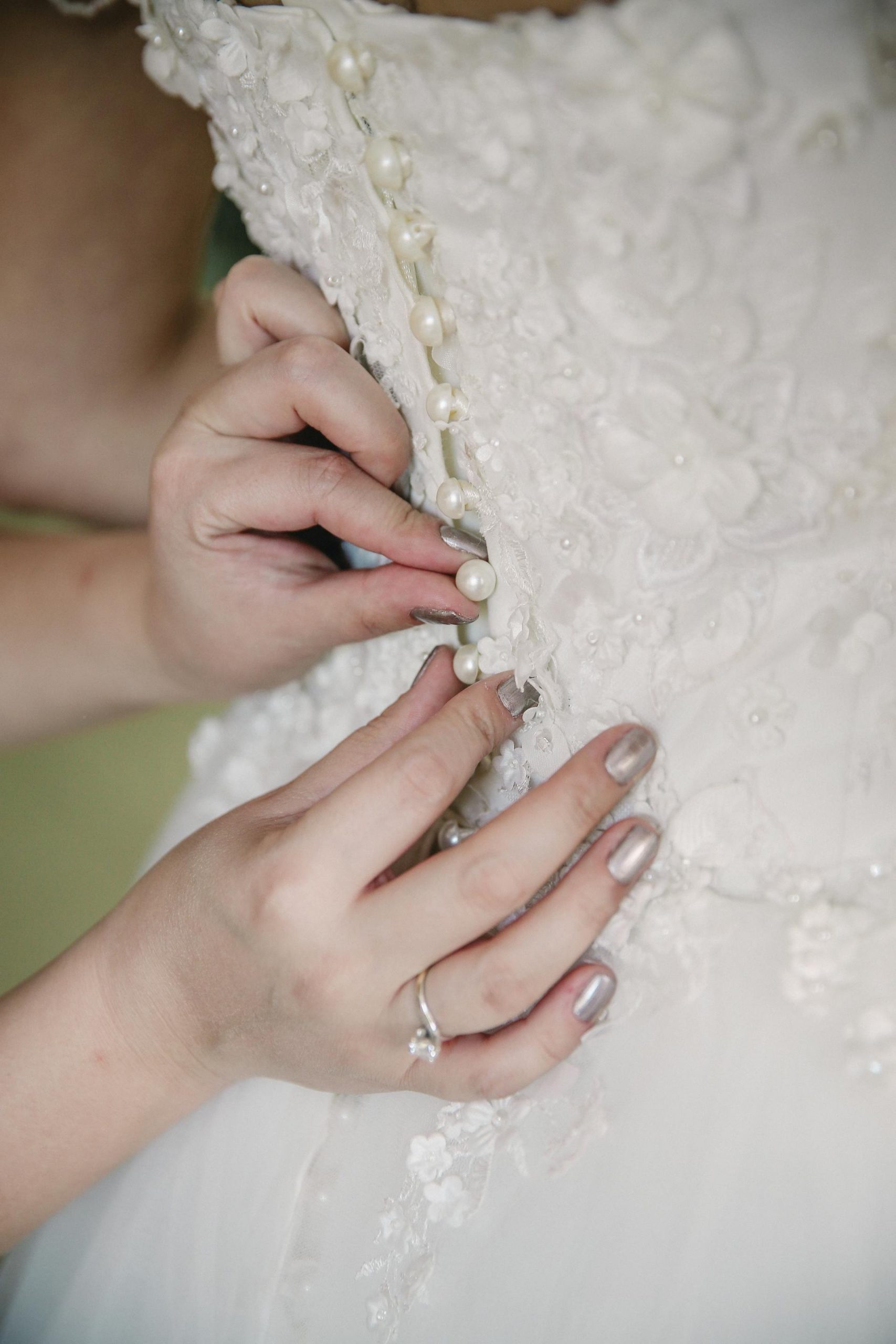 Hands buttoning up a bridal gown | Source: Pexels