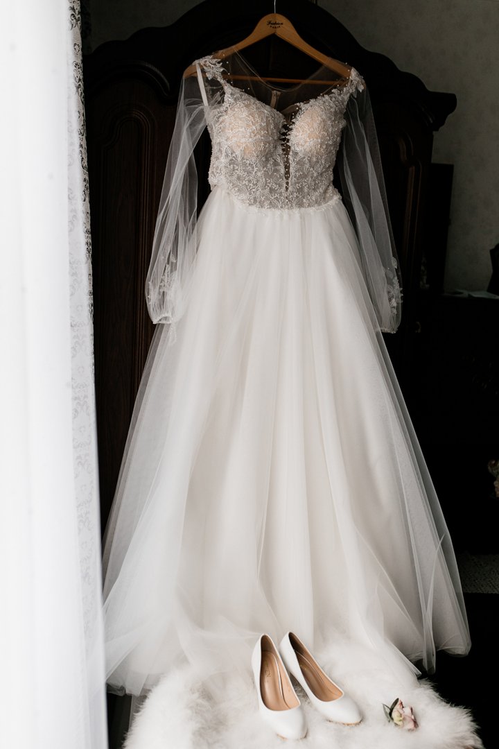 A bridal dress in a hanger and white heels lying on a fur pouf | Source: Freepik