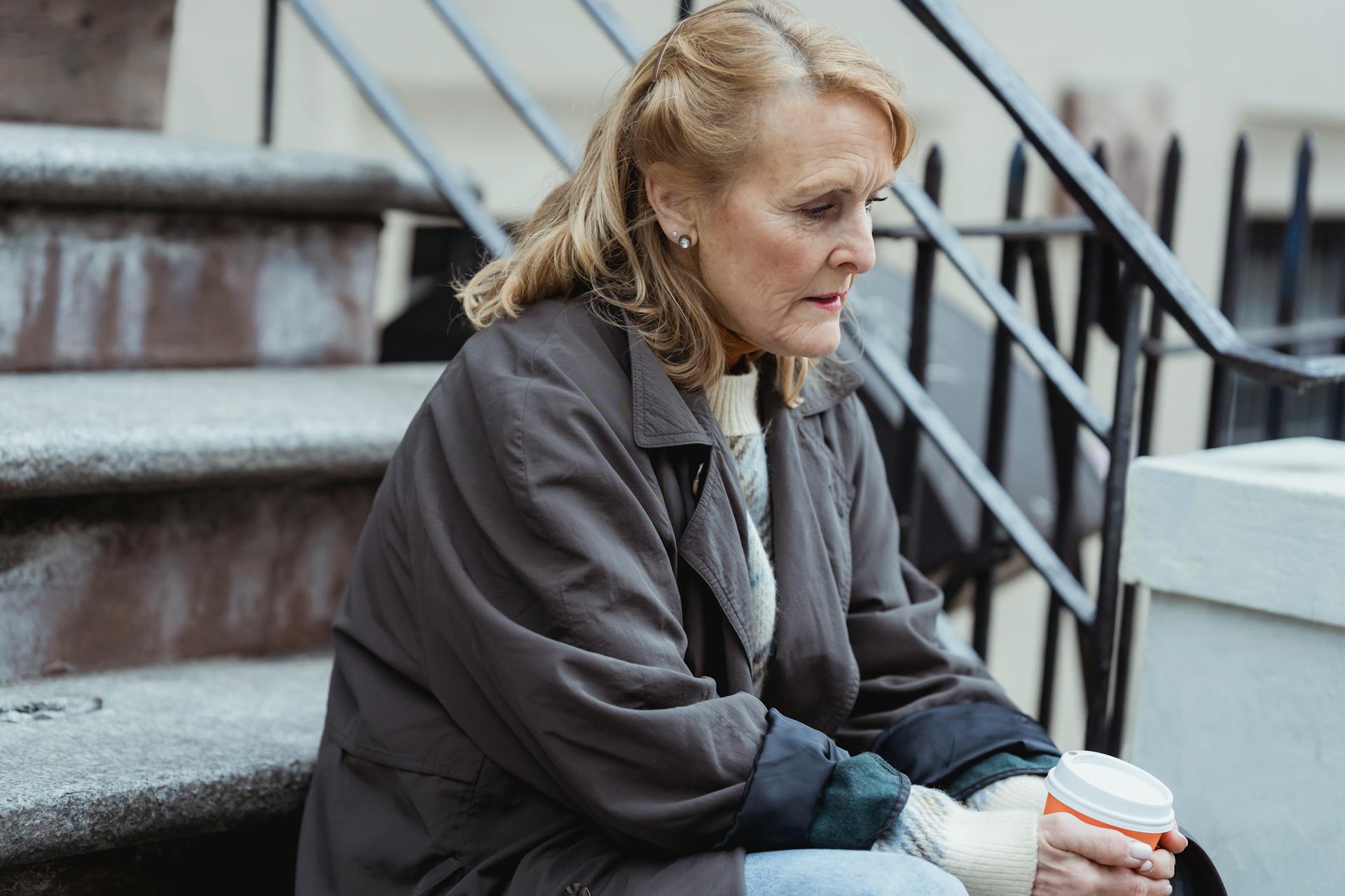 A wistful woman with takeaway coffee sitting on a staircase | Source: Pexels