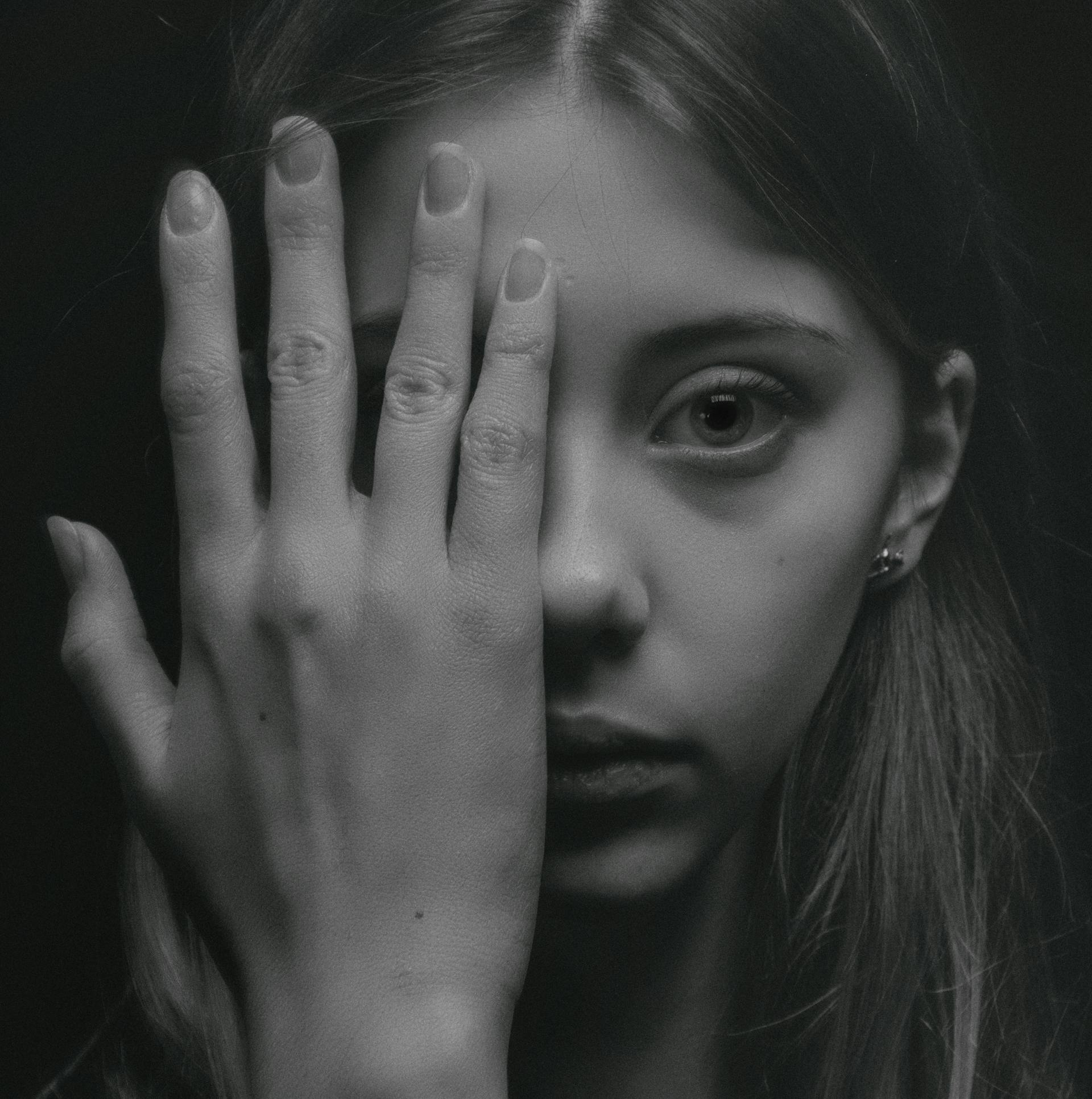 A grayscale photo of a young woman covering half of her face with her hand | Source: Pexels