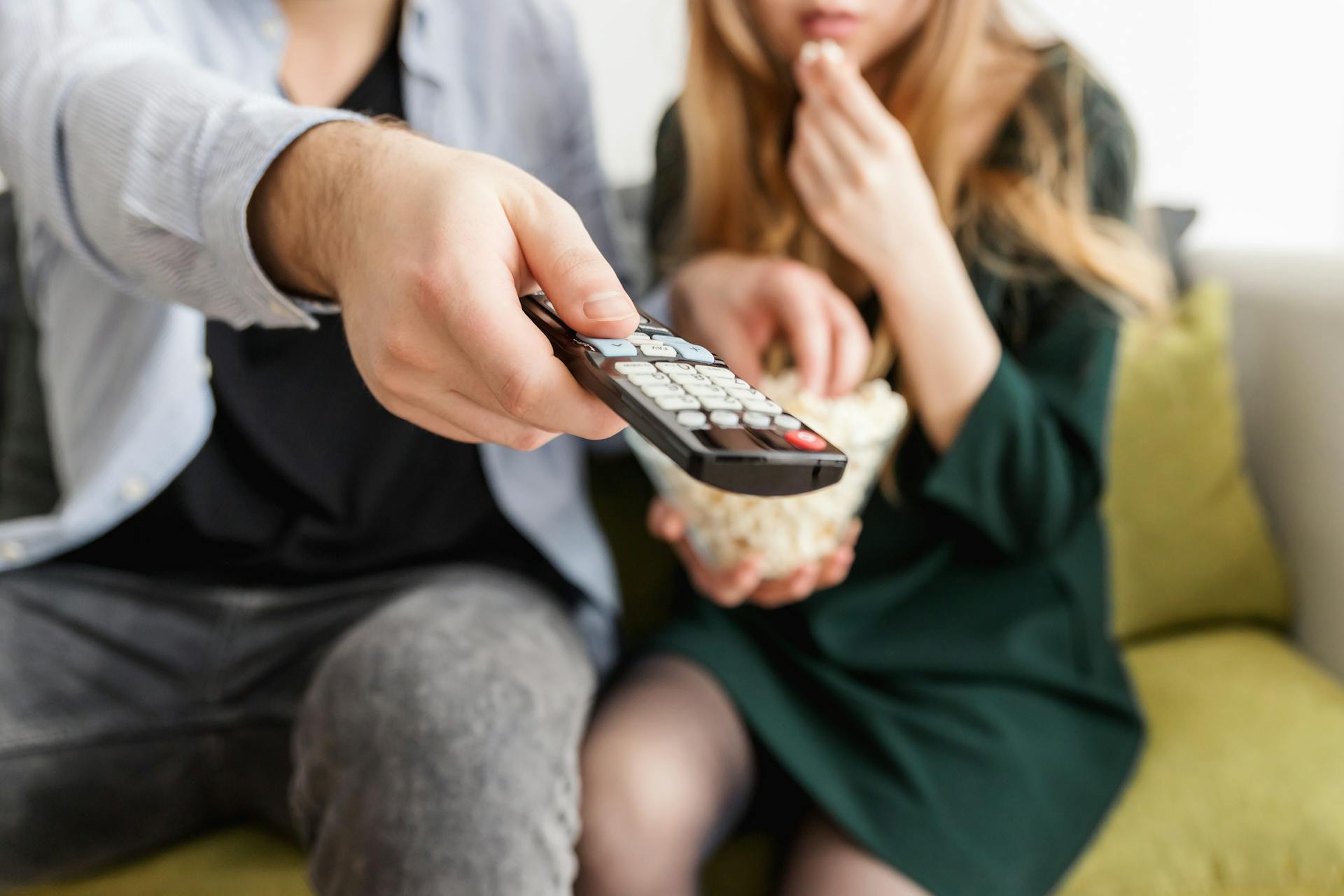 A man holding a remote control while eating popcorn with his wife | Source: Pexels