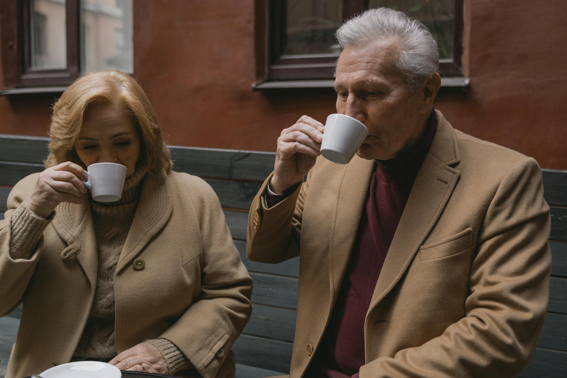 A senior couple drinking coffee while sitting on a bench | Source: Pexels