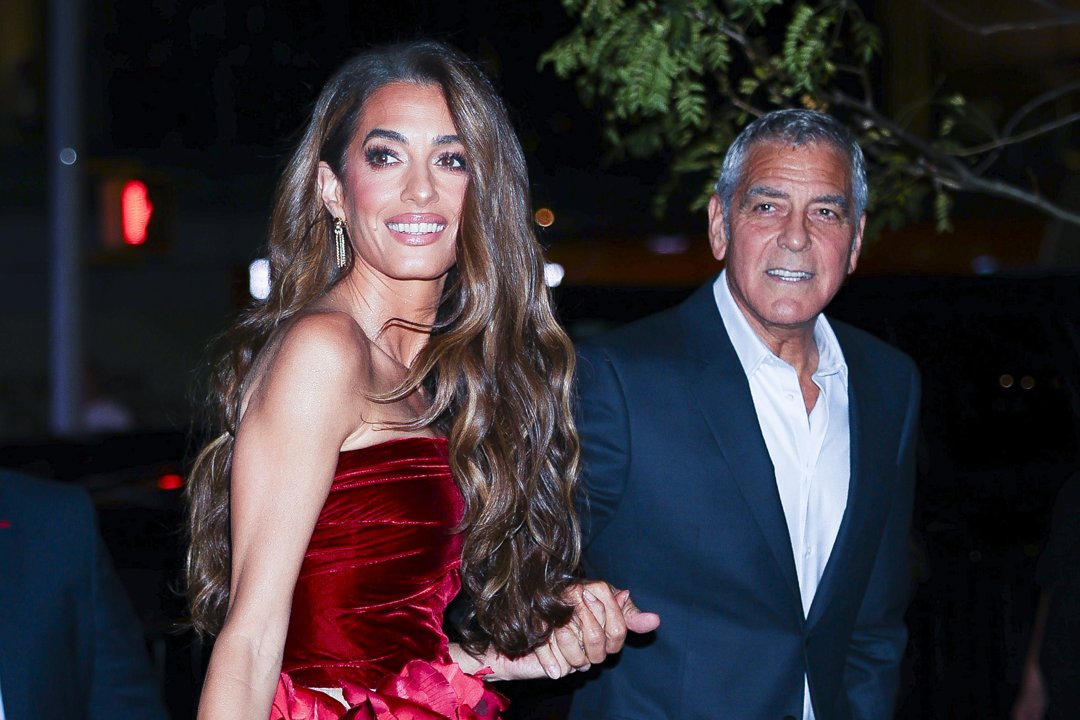 Smiling confidently, Amal Clooney glows beside George Clooney under the city lights. Her voluminous hair and vivid gown stealing the spotlight before they even reach the carpet.