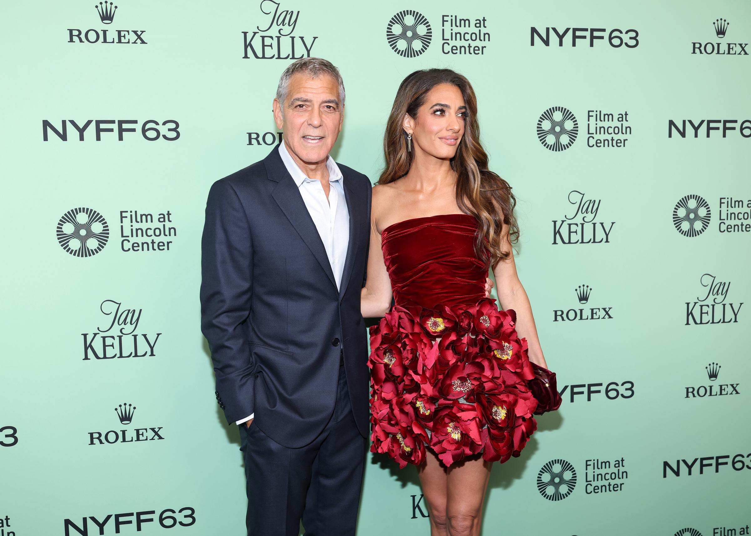 In a wide-angle shot against the festival backdrop, George Clooney and Amal Clooney pose confidently, their red carpet chemistry captured in a perfectly balanced frame.