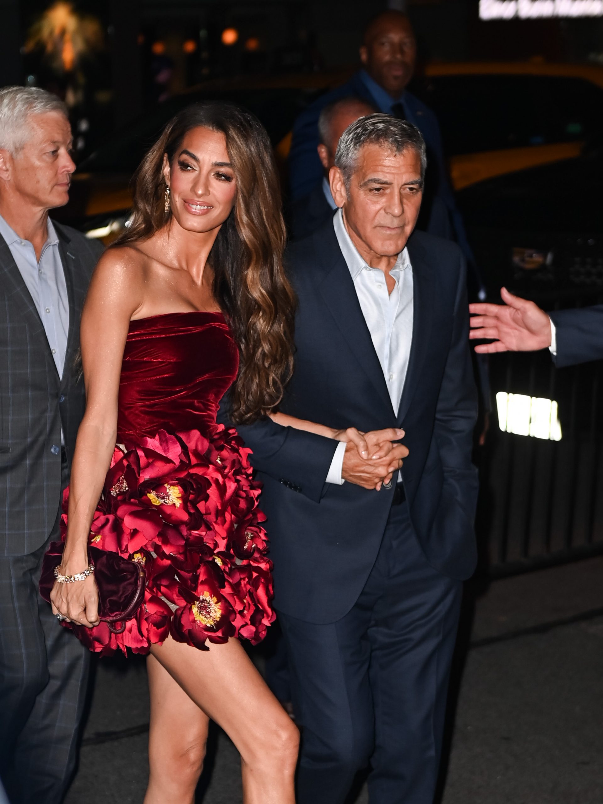 Amal Clooney locks arms with George Clooney as they make their entrance, her soft smile and flowing hair capturing attention before the cameras even start flashing.