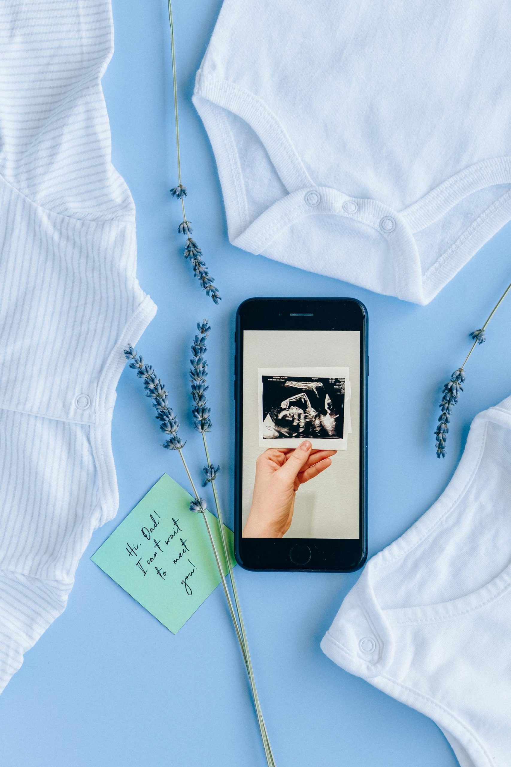 A sonogram on a phone screen beside baby clothes | Source: Pexels