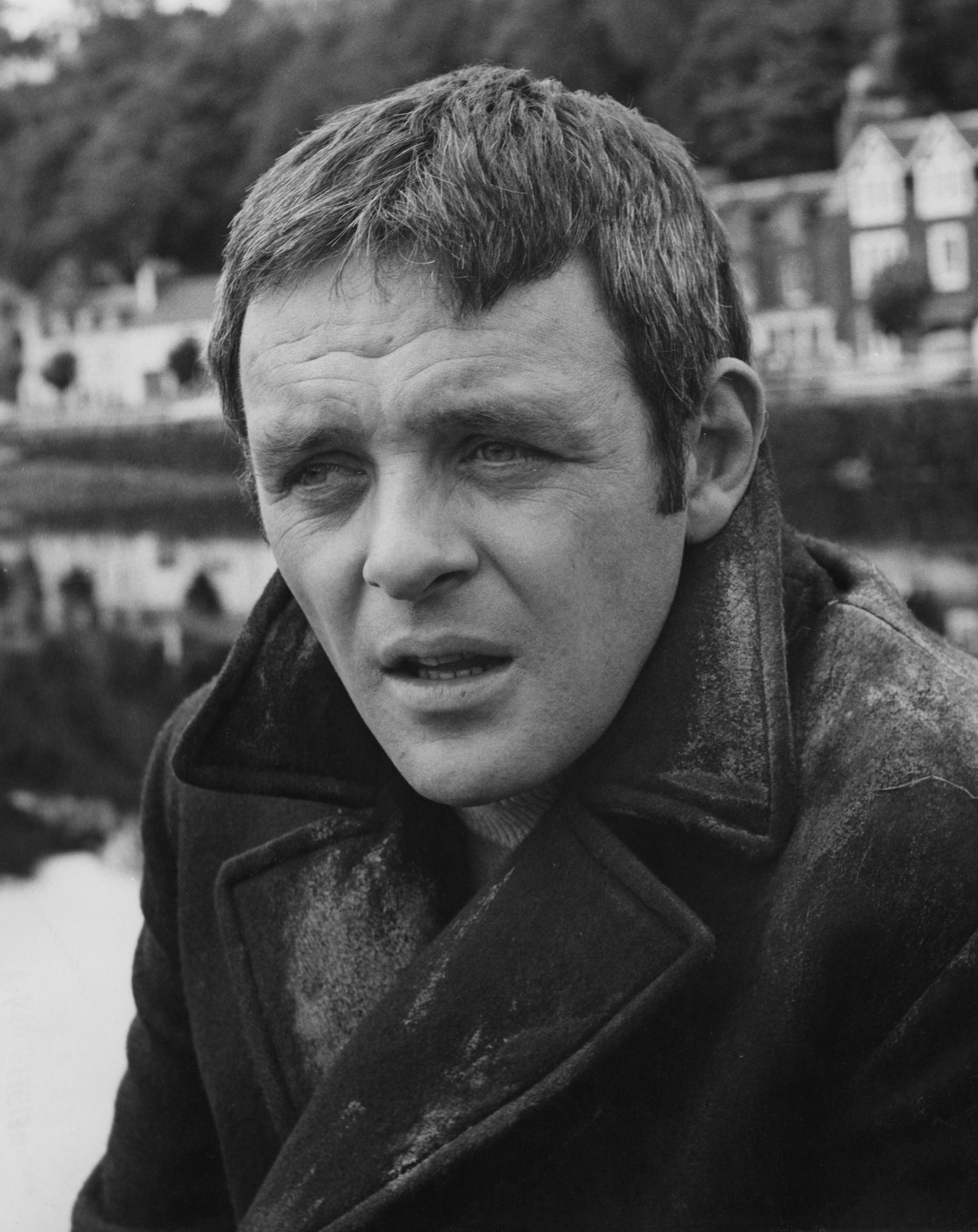 Gazing into the distance, Anthony Hopkins's expression is between contemplation and quiet sorrow. The textured coat and misty backdrop evoke a mood of solitude and reflection. Every detail in the monochrome scene speaks of depth, restraint, and the weight of unspoken emotion.