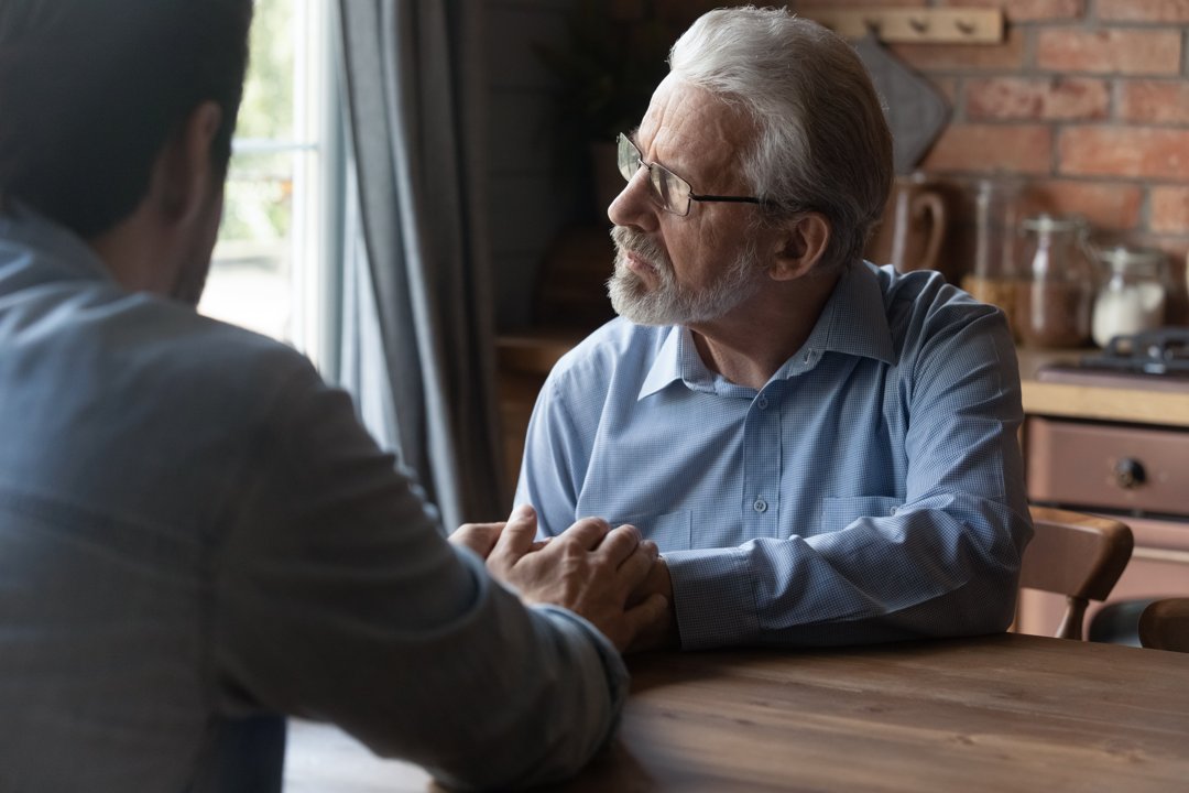 An adult son sitting with his stressed father | Source: Shutterstock