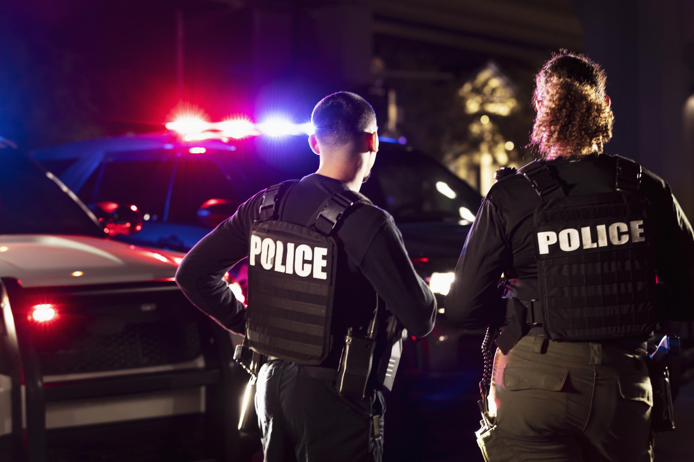 Two police officers standing side by side in front of their police vehicles. | Source: Getty Images