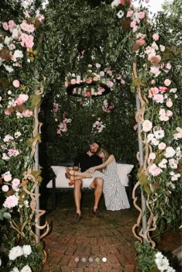 Travis Kelce and Taylor Swift posing under a floral archway on their engagement day, posted on August 26, 2025. | Source: Instagram/taylorswift