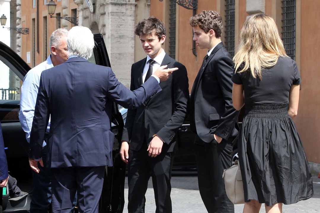 Richard Gere points as he steps out of a vehicle in Vatican City, guiding son Homer Gere and partner Alejandra Silva during their arrival at a formal event near Paul VI Hall, all dressed sharply in black.