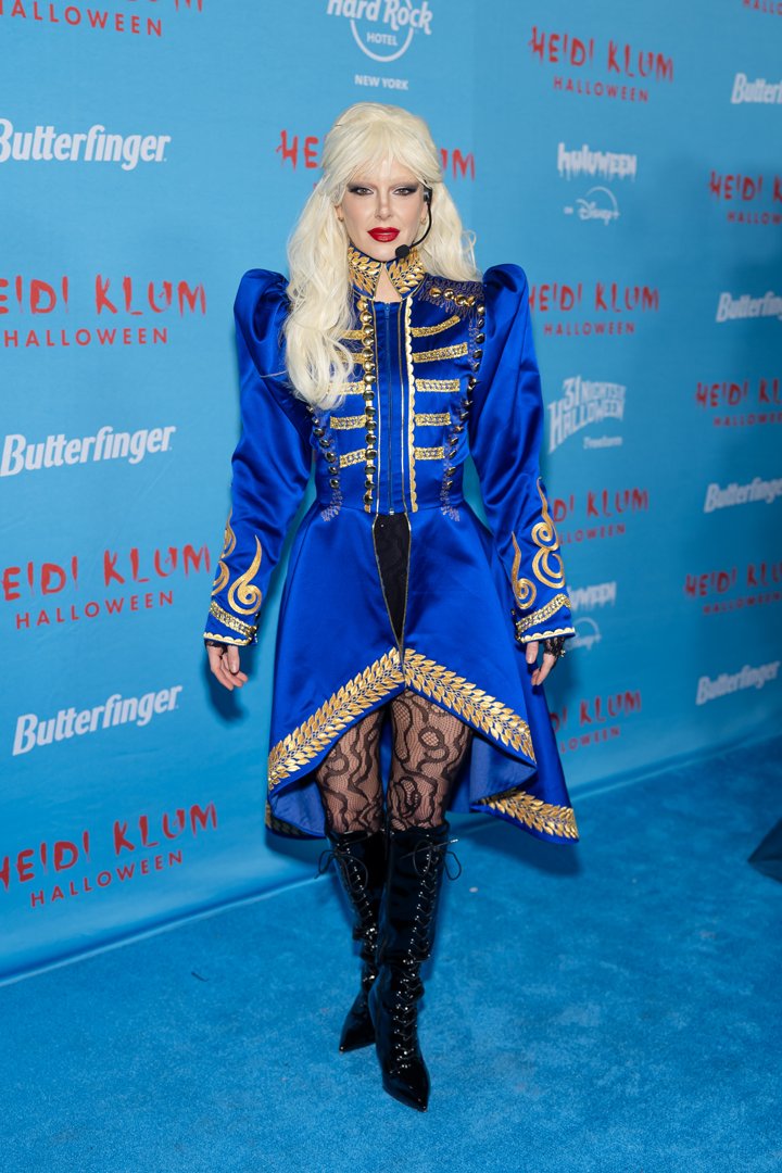 At Heidi Klum's 24th Annual Halloween Party on October 31, 2025, in New York, Madix brought bold stage presence in a dazzling blue and gold ensemble reminiscent of a pop star on tour. Her costume featured a military-style coat with sharp shoulders, gold detailing, and a high-low hem trimmed in laurel embroidery. She paired it with patterned black lace tights, patent lace-up boots, and a platinum blonde wig with fringe. A headset microphone completed the performance-ready look, channeling glam and authority in equal measure.