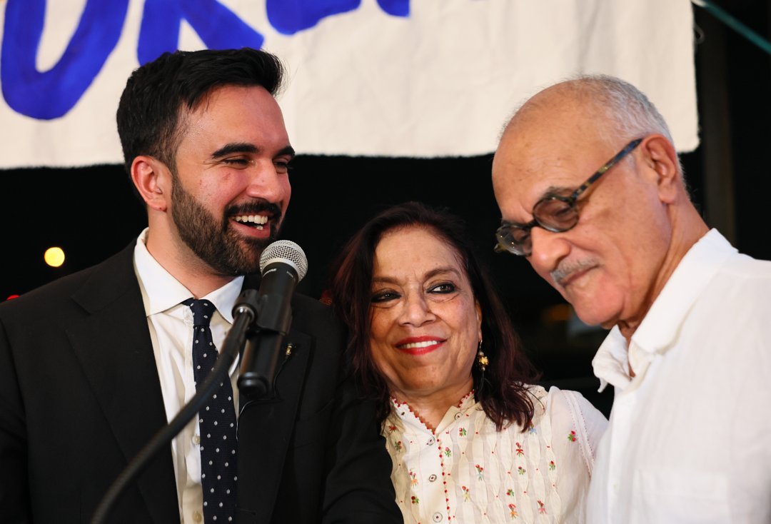 Zohran Mamdani stands with his mother Mira Nair, and father Mahmood Mamdani as they celebrate during an election night gathering at The Greats of Craft LIC in New York on June 24, 2025. | Source: Getty Images