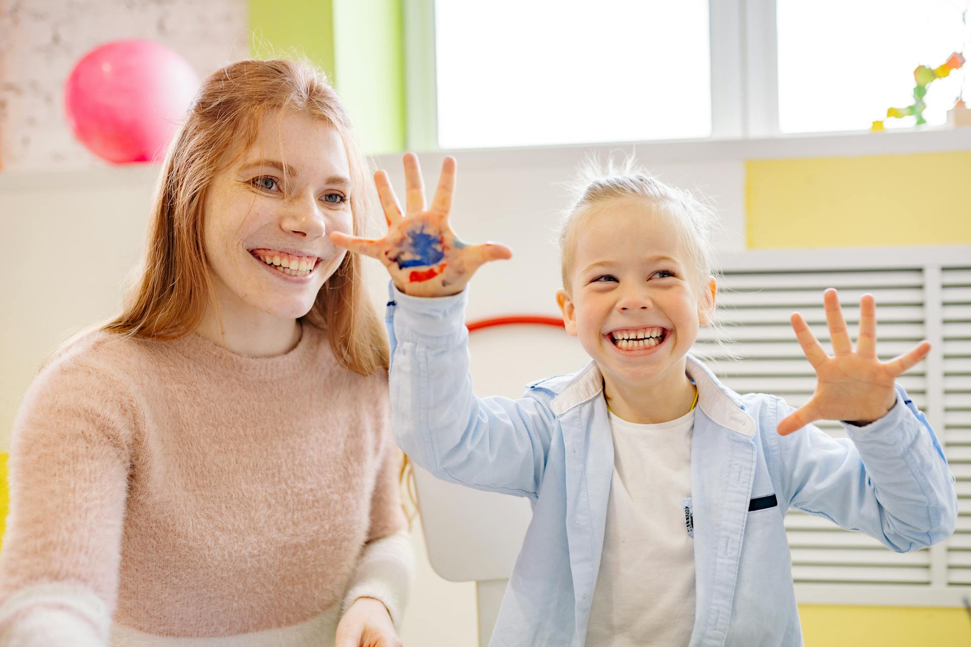 A woman sitting beside a little girl with paint on her hand | Source: Pexels