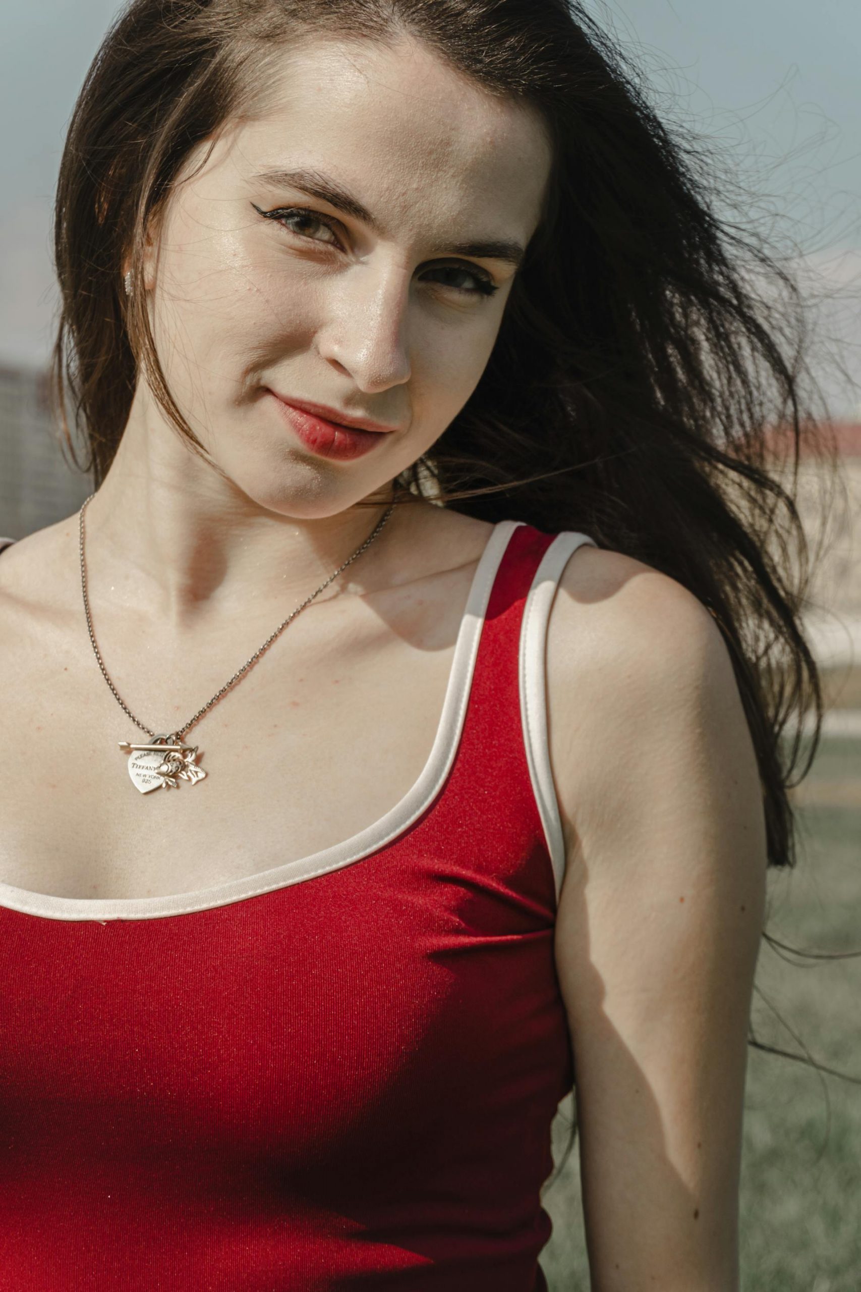 A woman in a red top smiling while standing outdoors | Source: Pexels