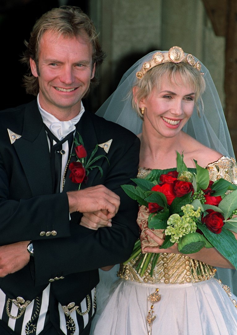 Trudie Styler, at 38, appeared with a serene, natural expression, featuring prominent, well-defined brows over her large eyes, a soft, slightly rounded jawline, and shoulder-length, subtly waved hair, as Sting held her prior to entering their village church for a marriage blessing on August 22, 1992, in Great Durnford, Wiltshire.