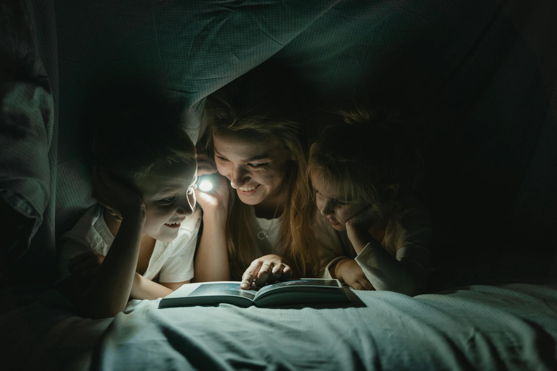 A woman holding a flashlight and reading a story to her kids | Source: Pexels
