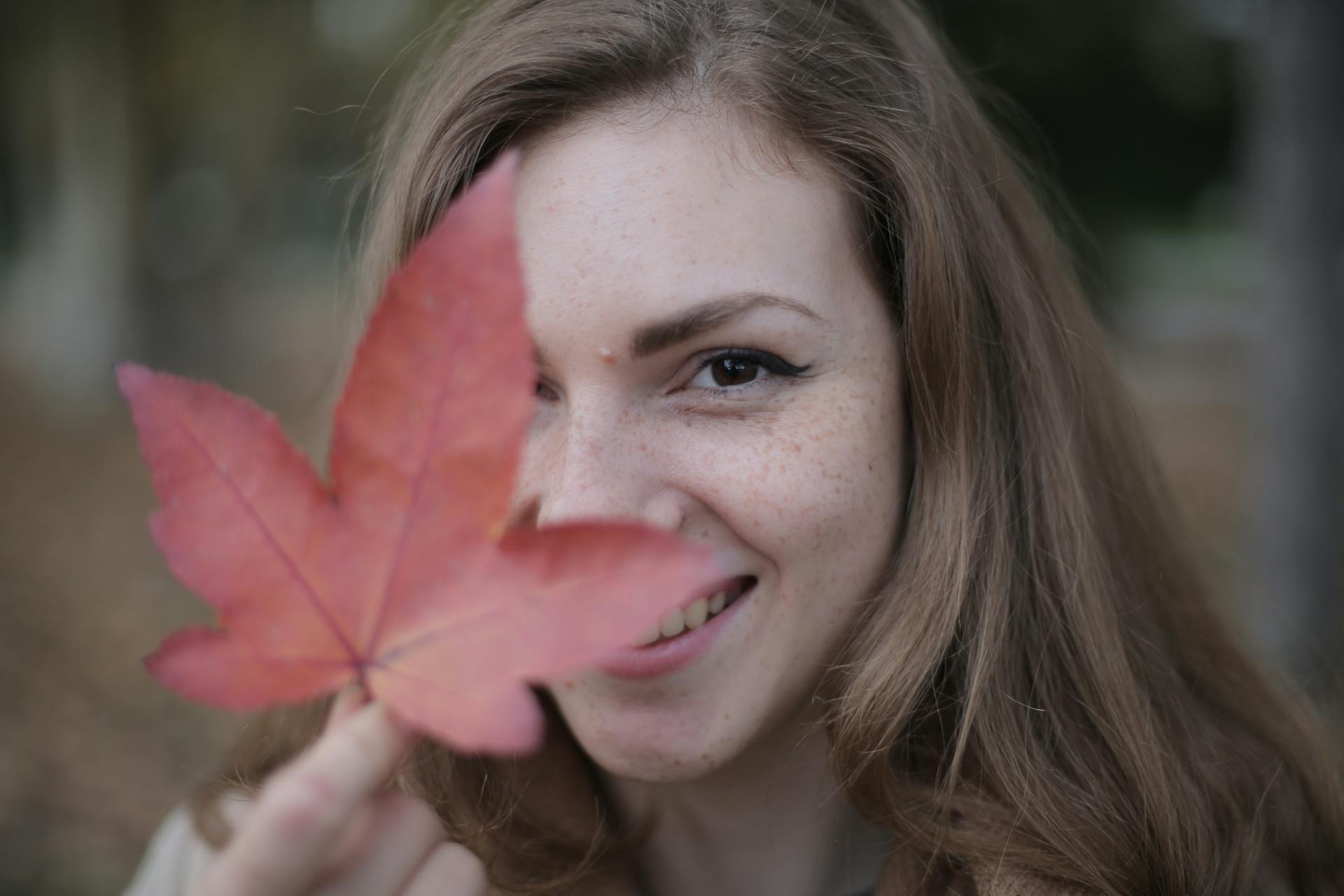 A young woman smiling while holding a maple leaf | Source: Pexels