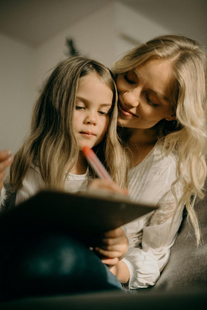 Girl writing on paper as her mother watches | Source: Pexels