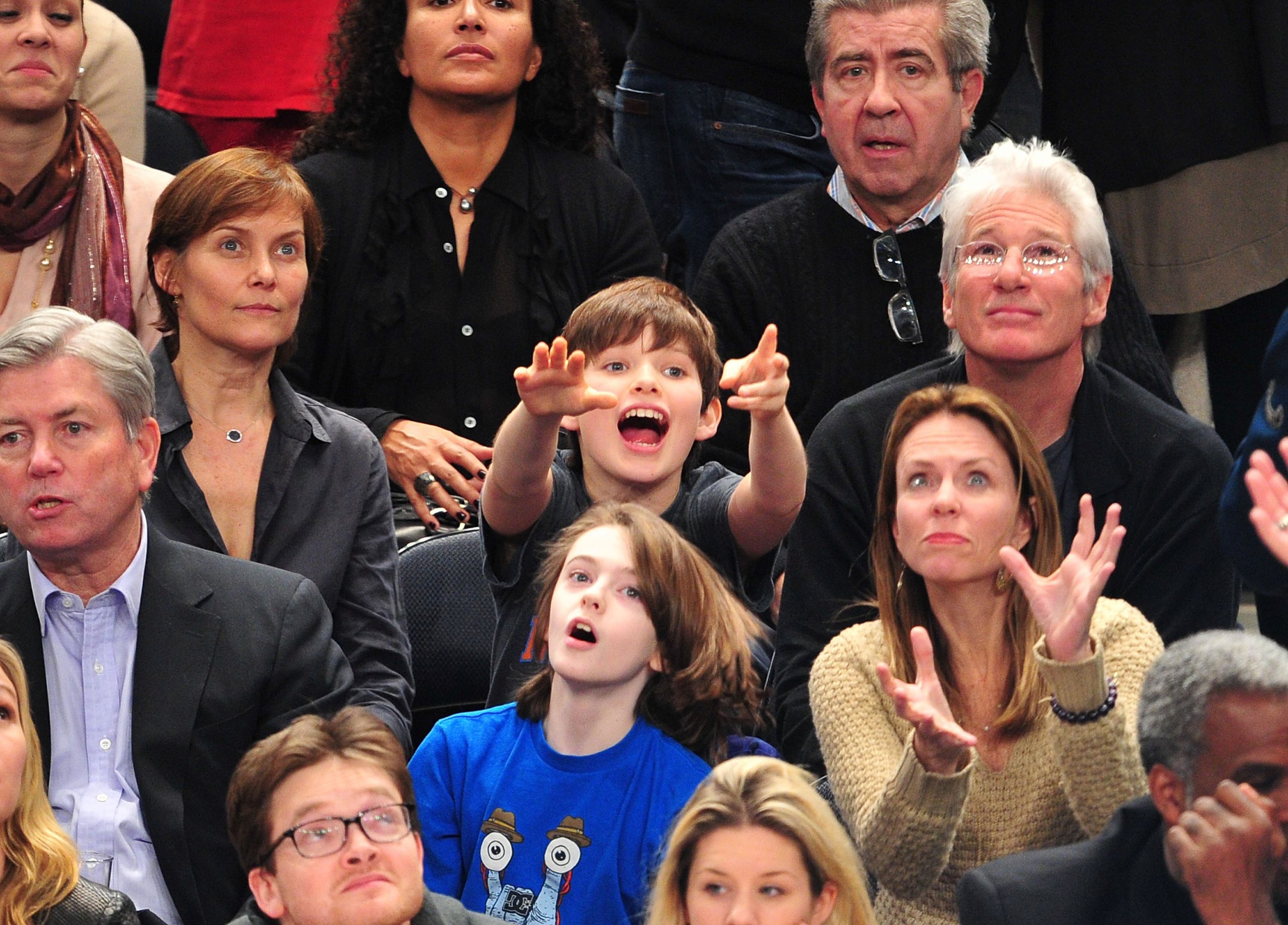 With excitement in his eyes, Homer Gere gestures toward the court as he watches the New York Knicks take on the Chicago Bulls at Madison Square Garden in New York City, seated beside his parents, Carey Lowell and Richard Gere.
