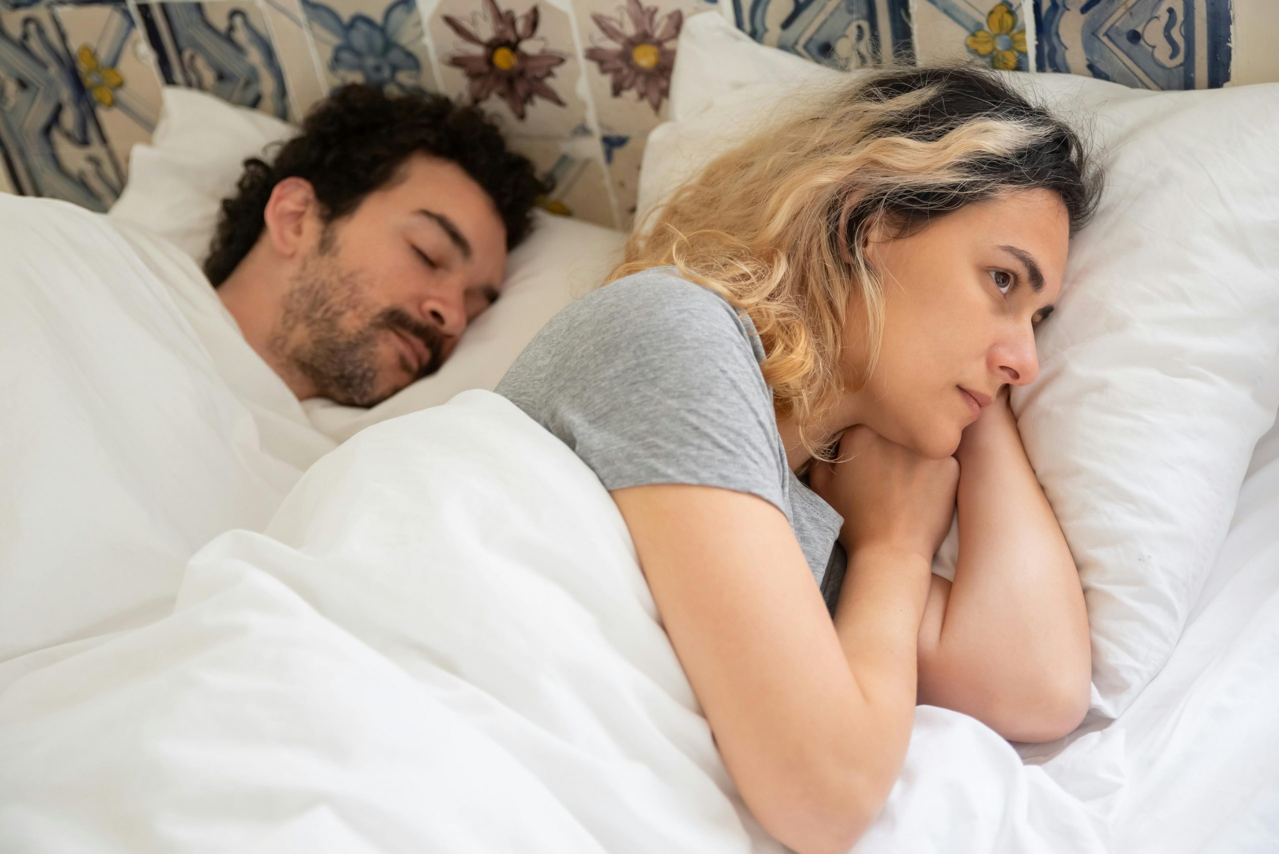 An upset woman lying awake in bed next to a sleeping man | Source: Pexels