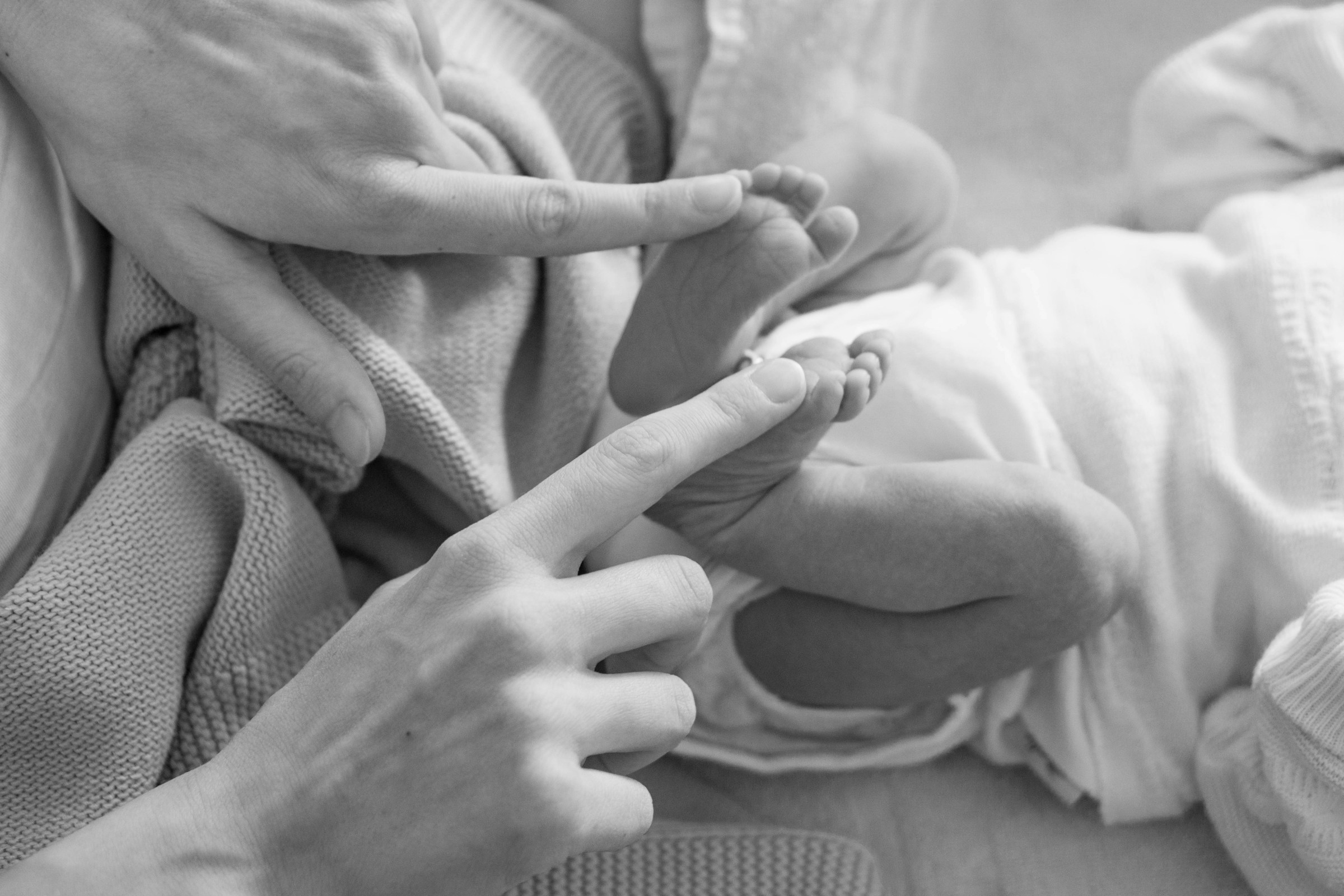 Grayscale photo of a mother touching her newborn baby's tiny feet | Source: Unsplash